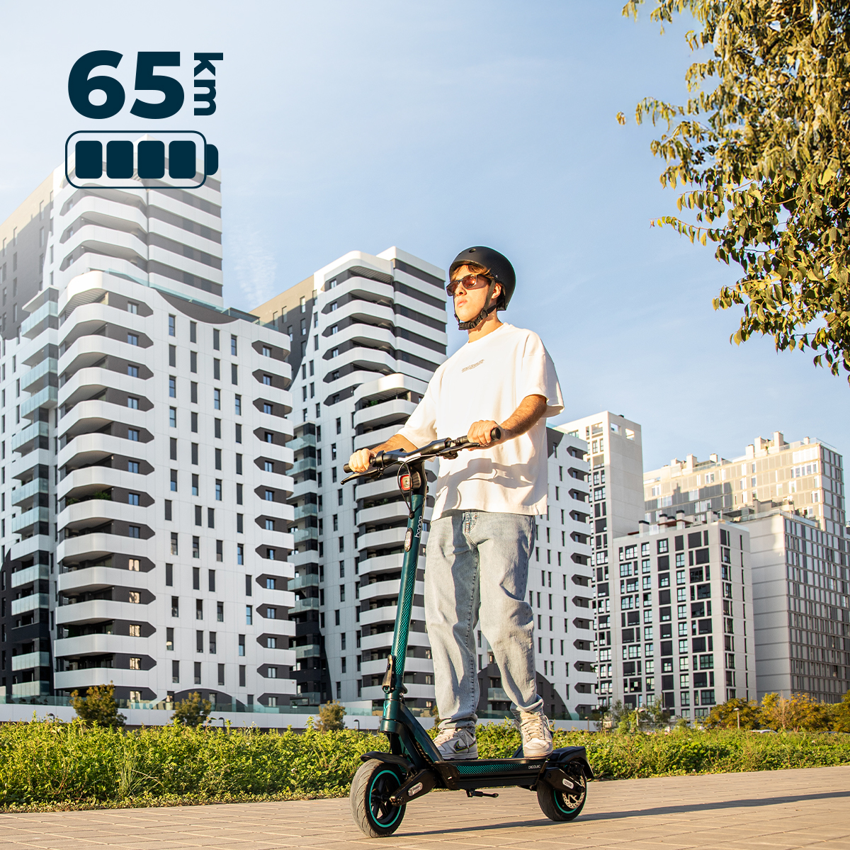 Un joven con casco y gafas de sol monta en patinete eléctrico frente a edificios modernos.