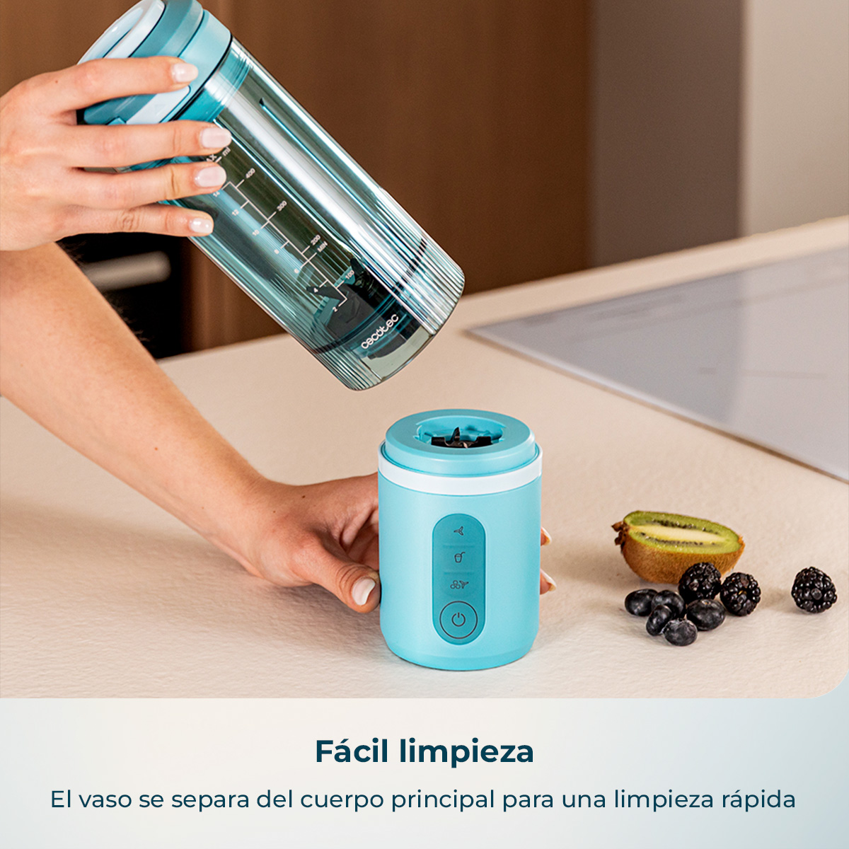 Una persona separa el vaso mezclador azul de la base en una encimera junto a kiwi y moras.