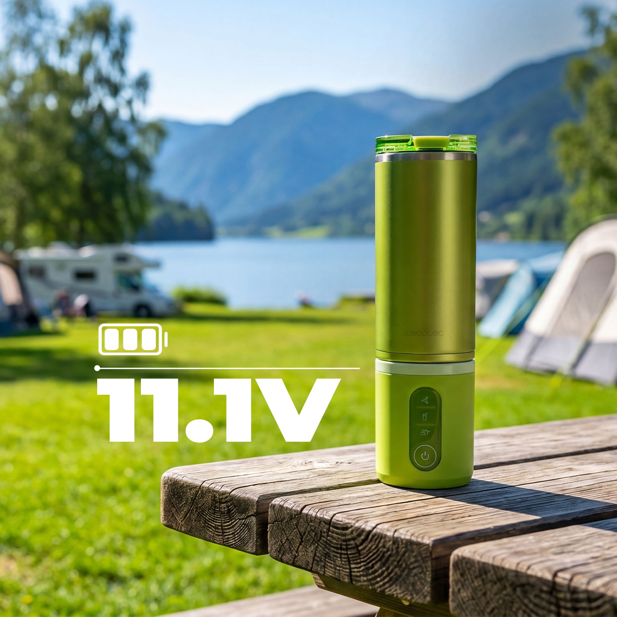 Una cafetera portátil verde sobre una mesa de picnic de madera al aire libre, con un lago y montañas de fondo.