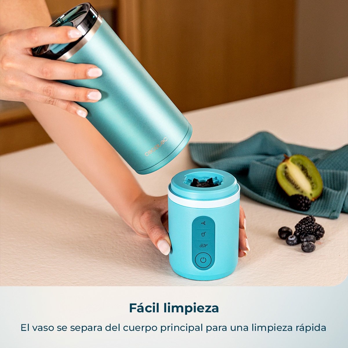 Una persona separando el vaso de una batidora portátil en una encimera de cocina con kiwi y bayas.