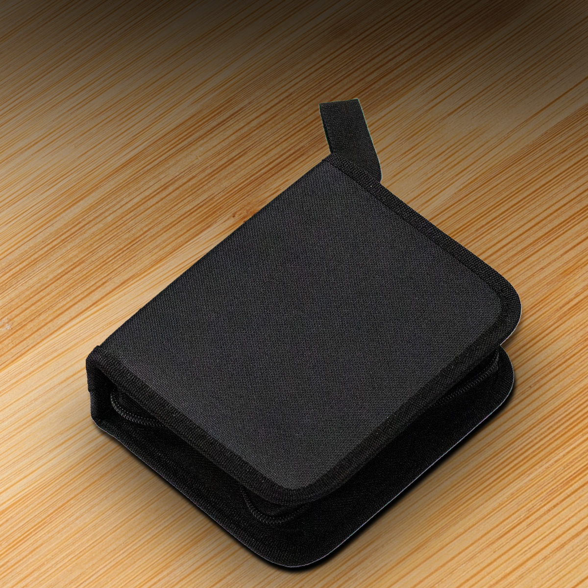 Un estuche de tela negra con cremallera cerrada descansa sobre una superficie de mesa de madera.
