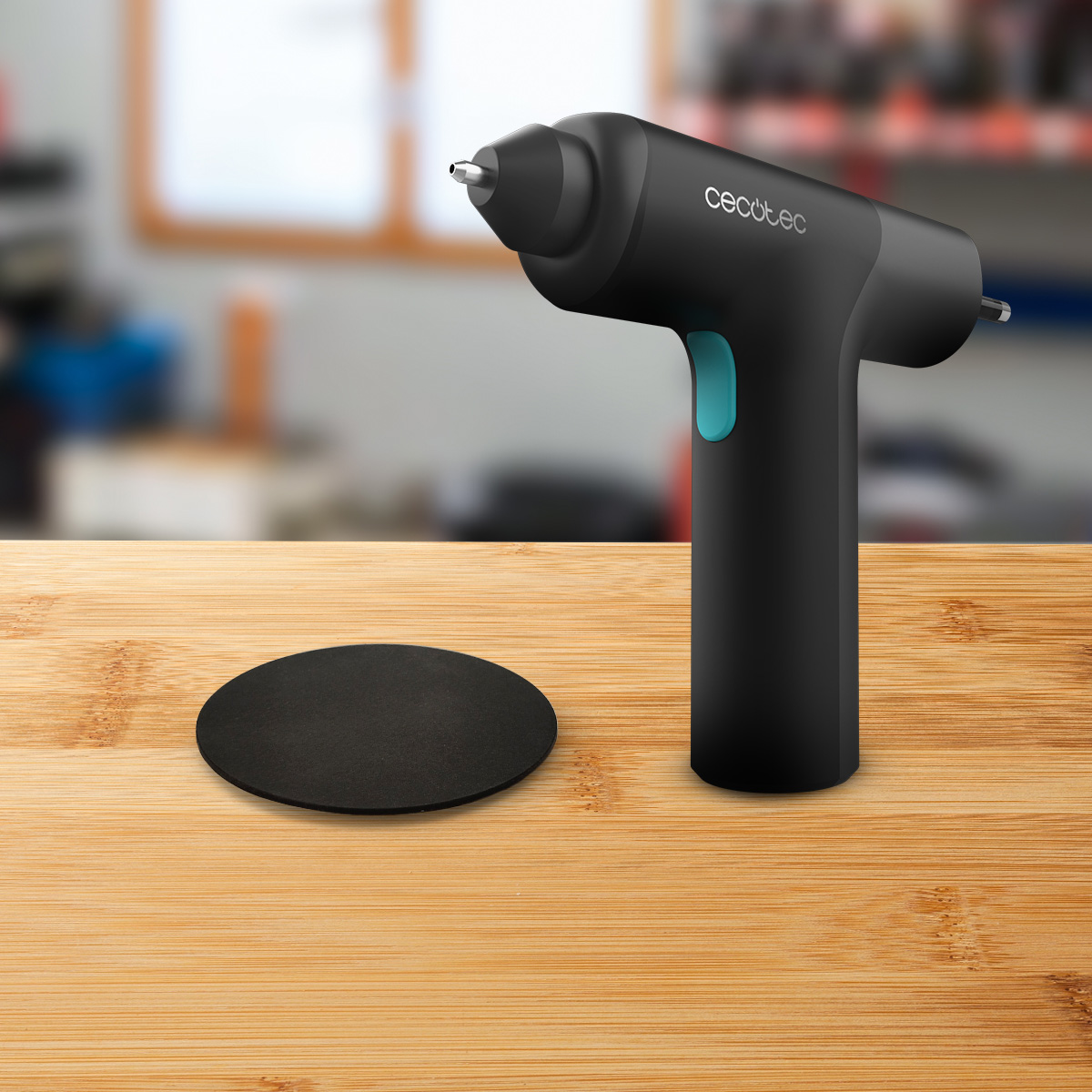 Una pistola de pegamento negra con gatillo azul y base circular en una mesa de madera.