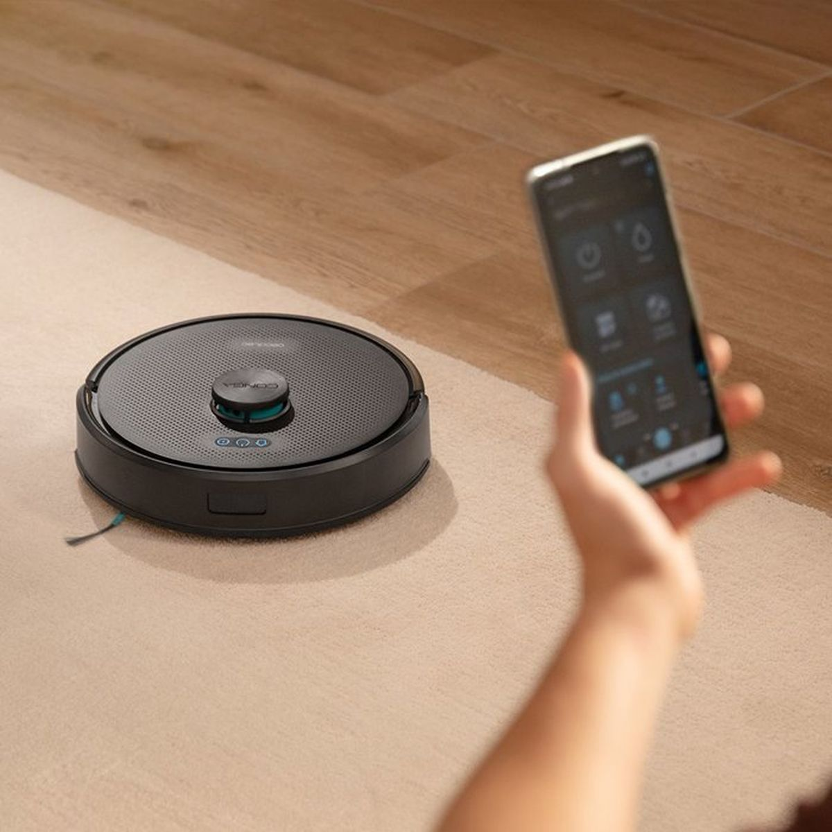 Un teléfono inteligente controla un robot aspirador negro en una alfombra.