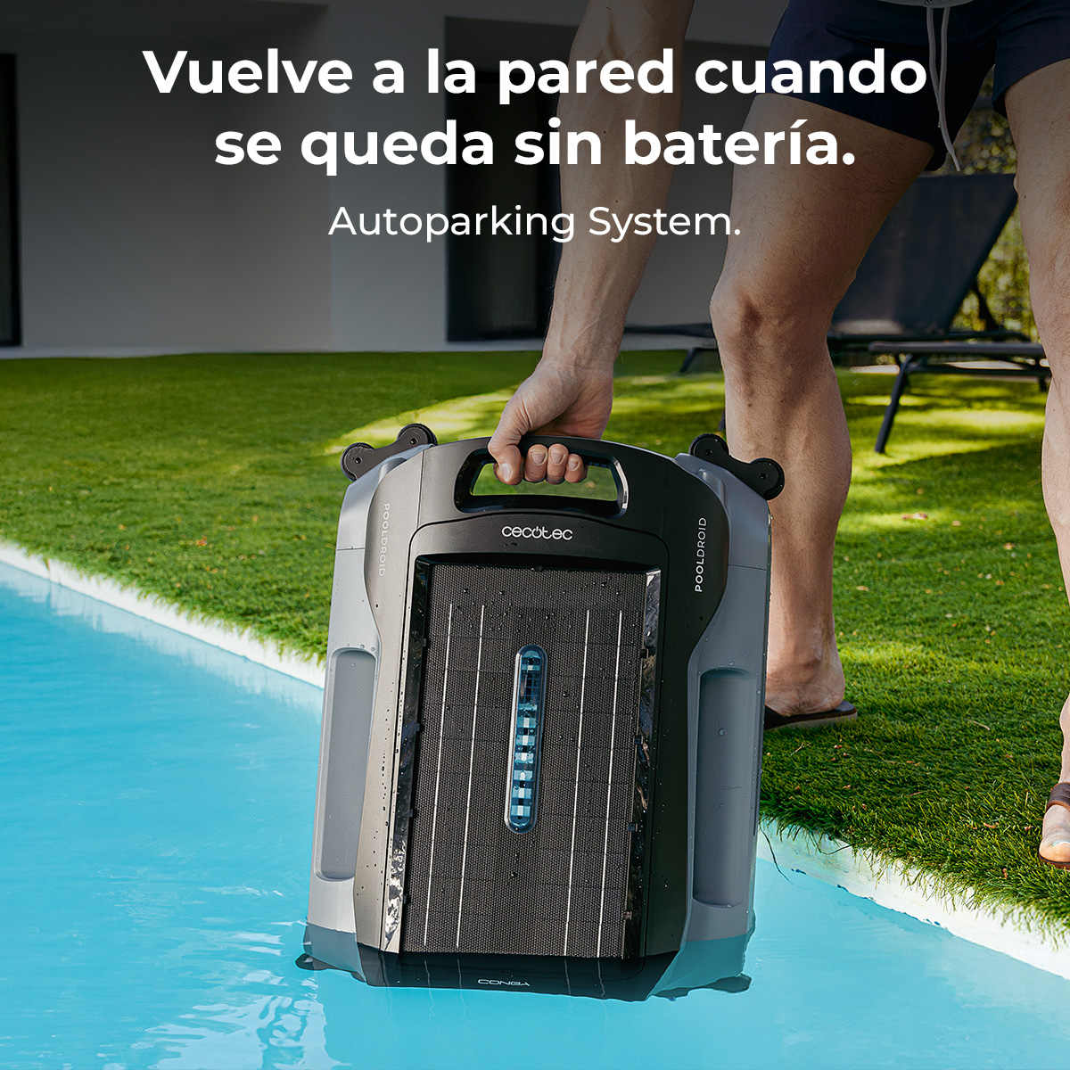 Una persona tiene in mano un pulitore per piscina grigio e nero vicino a un prato.