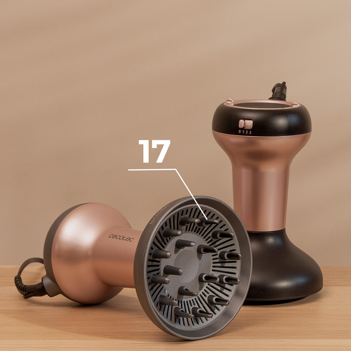 Dos secadores de pelo de oro rosa y negro con difusor sobre una superficie de madera con fondo beige.