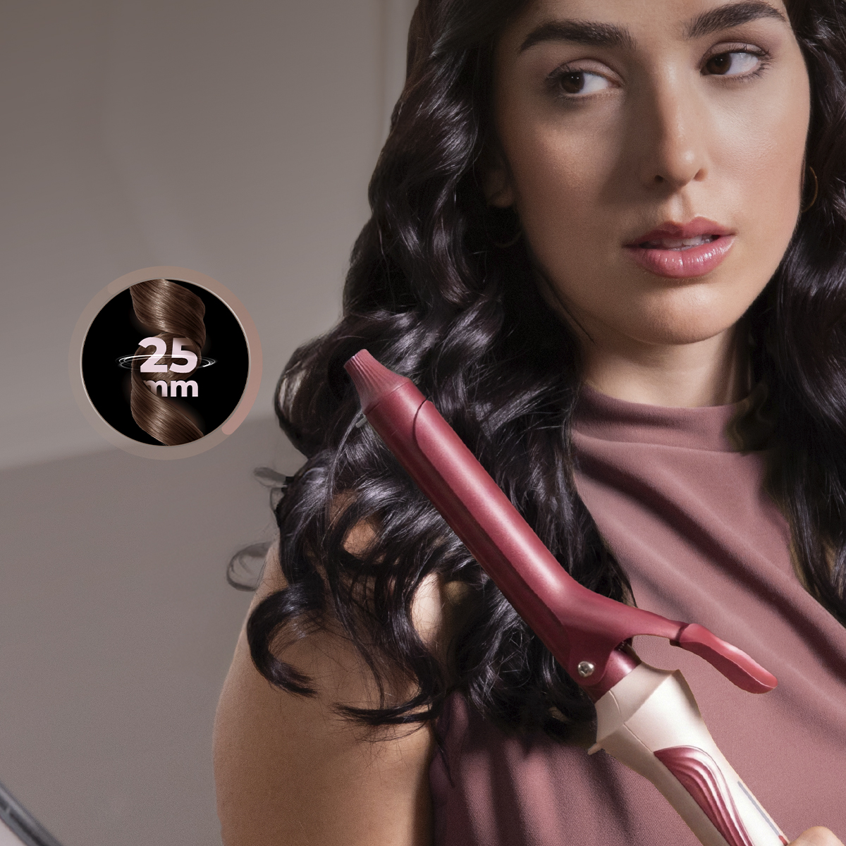 Una mujer con cabello oscuro sostiene un rizador rojo con un tamaño de rizo de 25 mm.