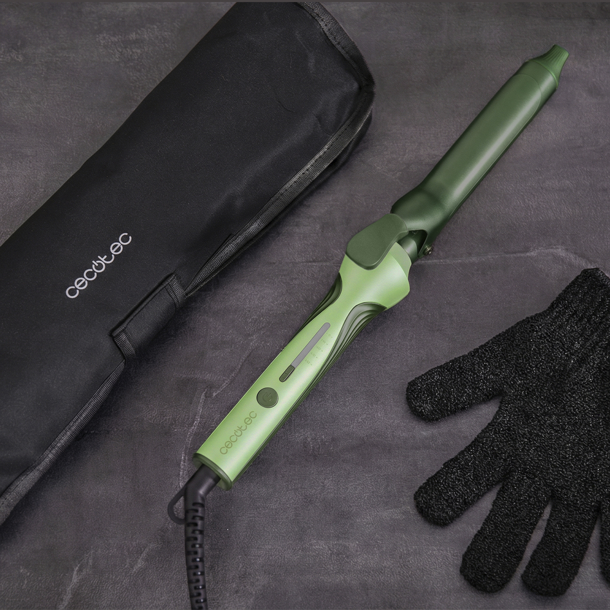 Un rizador verde está sobre una superficie oscura junto a una bolsa negra y un guante protector.