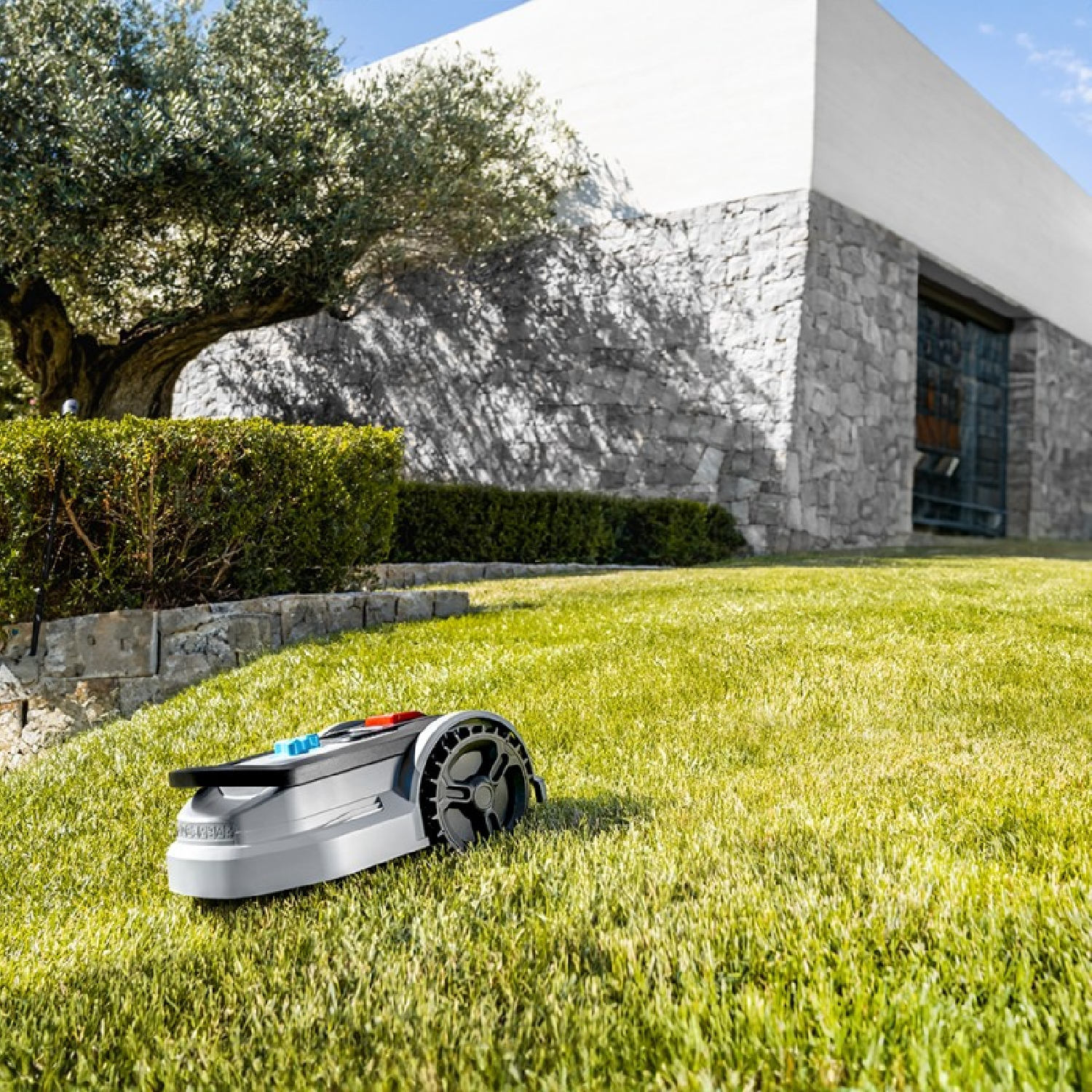 Un cortacésped robótico automático corta el césped verde frente a una casa moderna con fachada de piedra.