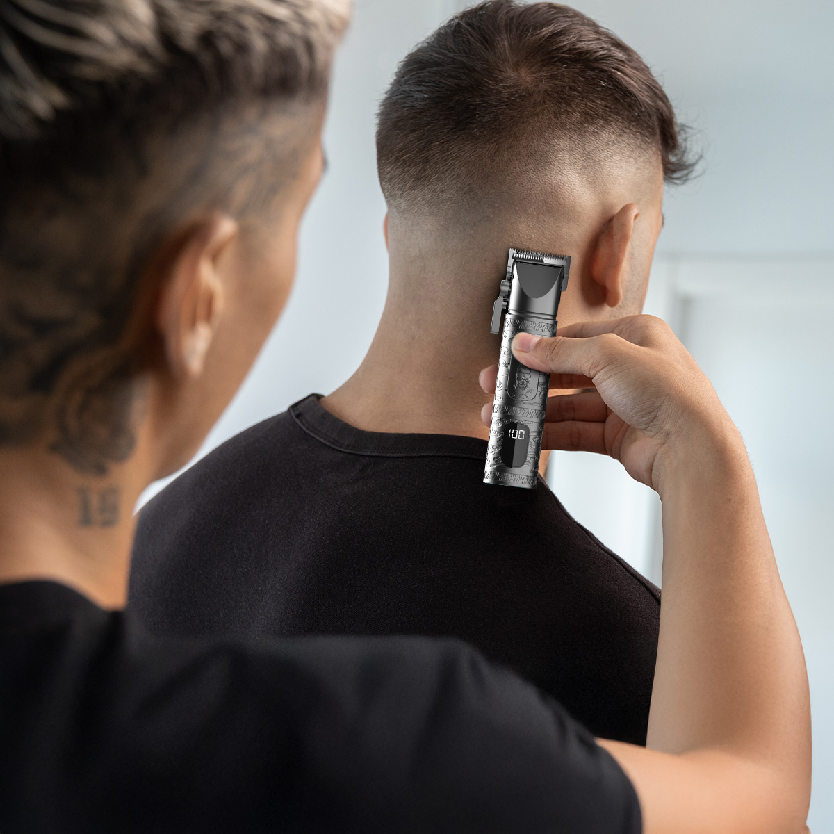 Una persona usa una máquina cortapelo plateada para recortar la nuca de otra persona.