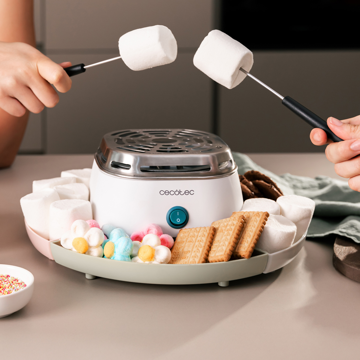 Due persone arrostiscono marshmallow su un piastra rotonda e bianca, circondata da biscotti.