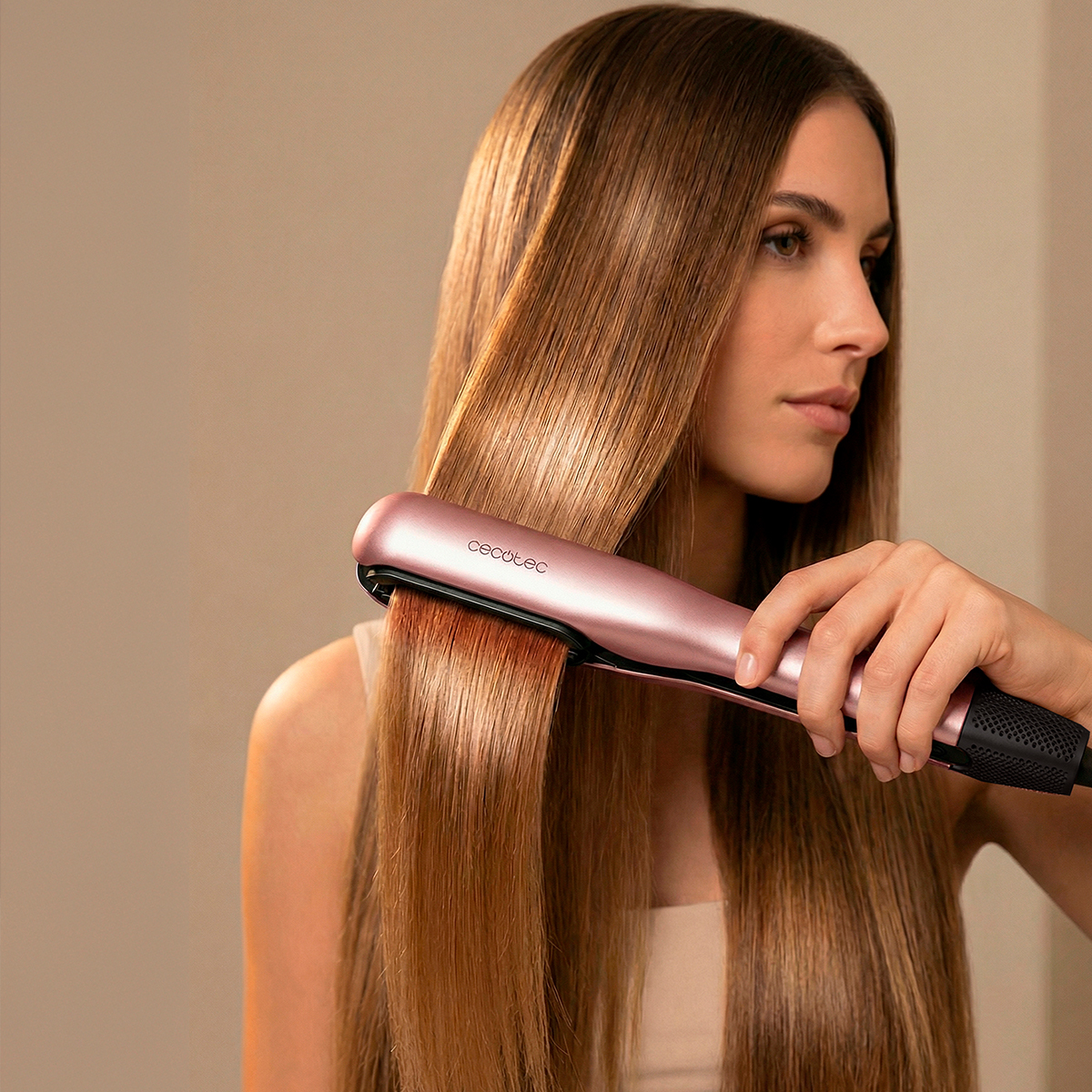 Una mujer alisa su largo y brillante cabello castaño con una plancha de pelo de oro rosa.