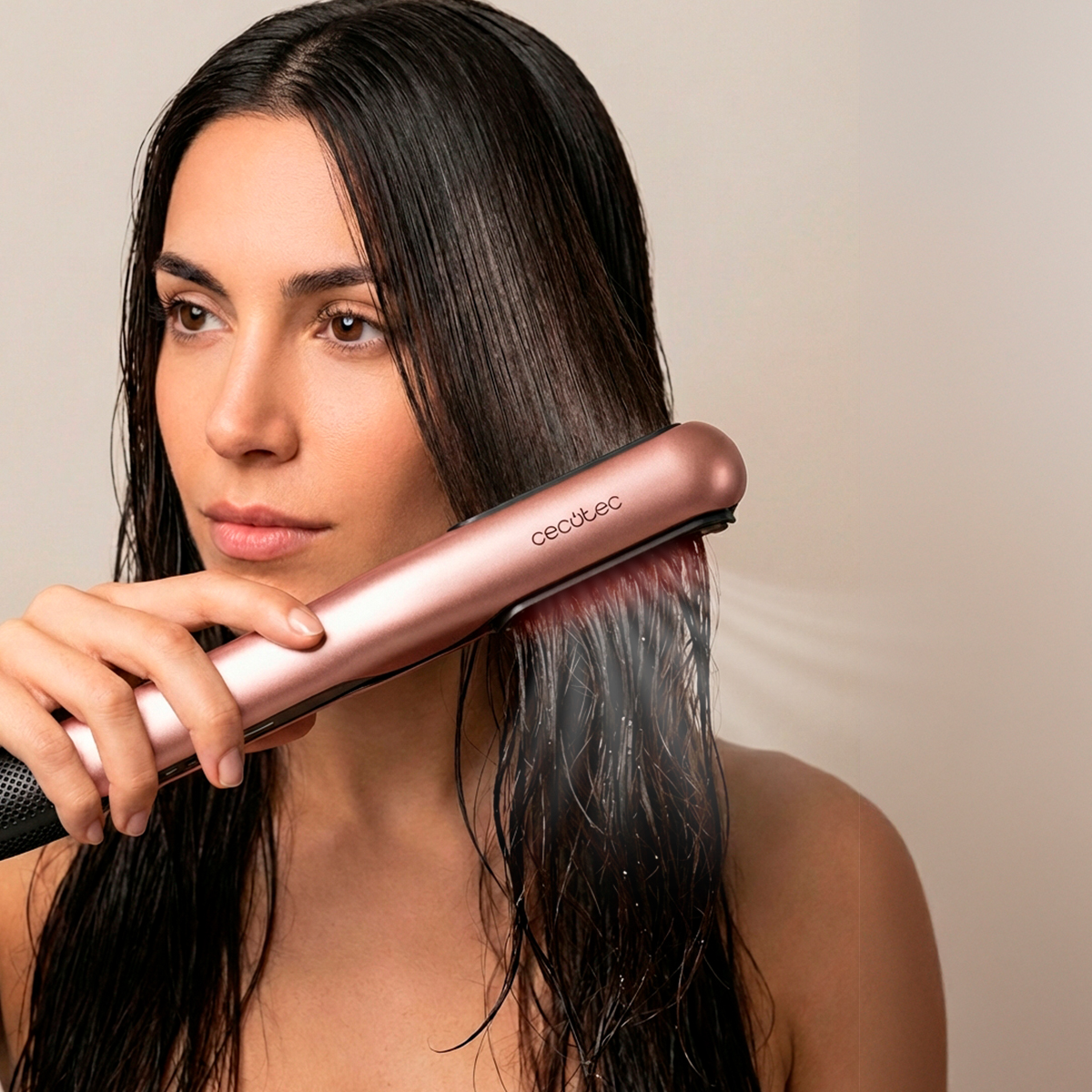 Una mujer alisa su cabello húmedo con una plancha de vapor de oro rosa sobre fondo liso.