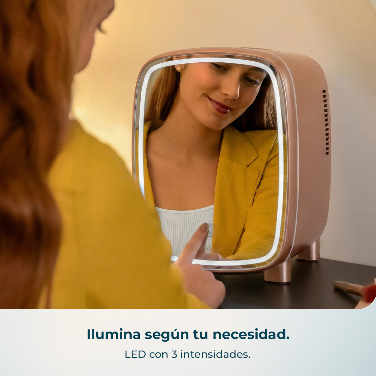 Una donna con giacca gialla usa uno specchio per trucco luminoso in oro rosa con controllo touch.
