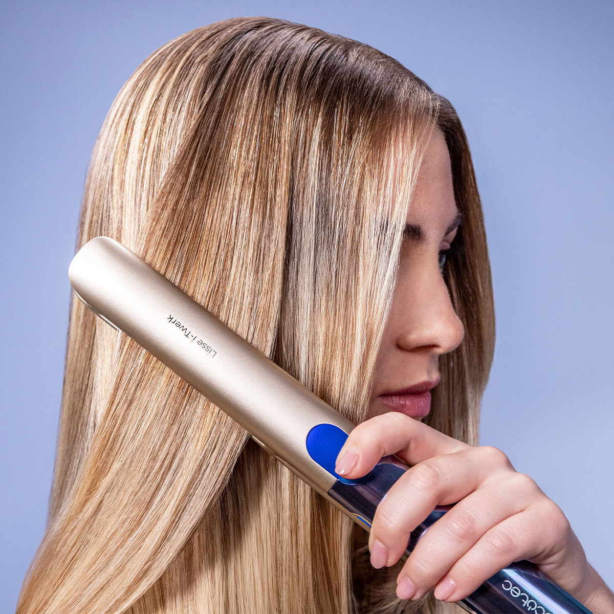 Una donna bionda usa una piastra per capelli dorata e blu su sfondo azzurro.
