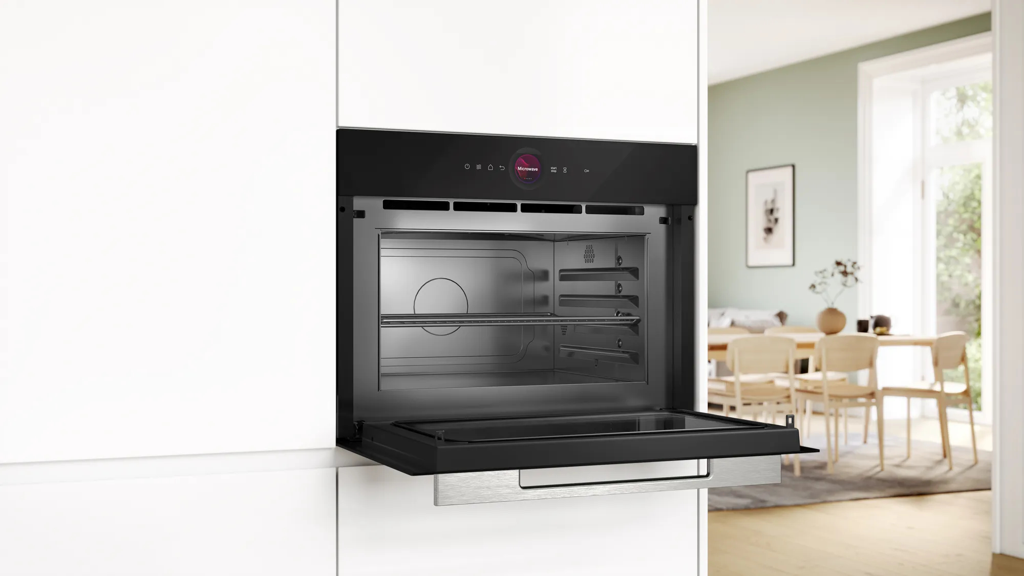 Un forno nero da incasso con la porta aperta in una cucina bianca, con una zona pranzo sullo sfondo.