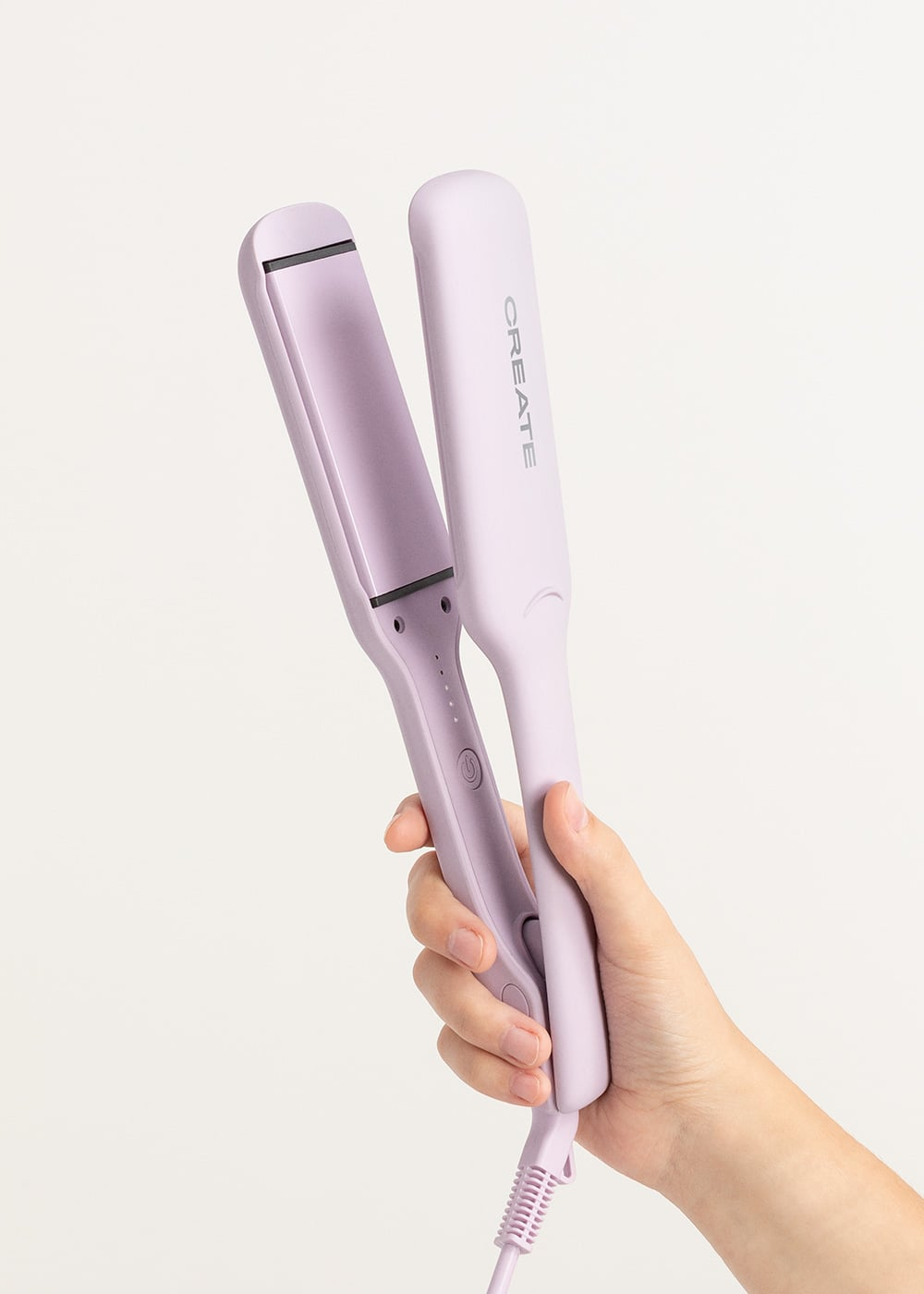 Una mano sostiene una plancha de pelo Create de color morado claro sobre un fondo blanco.