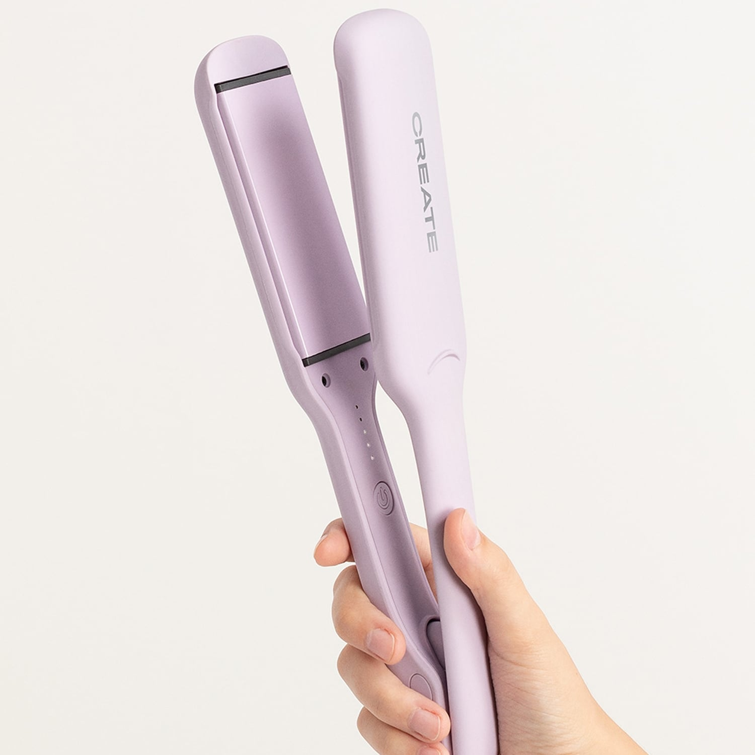 Una mano sosteniendo una plancha de pelo Create de color lila claro sobre fondo blanco.