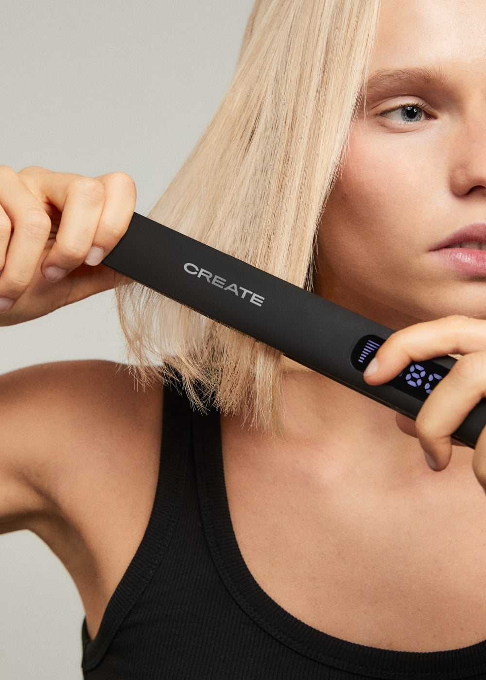 Una mujer rubia alisándose el pelo con una plancha de pelo negra CREATE.