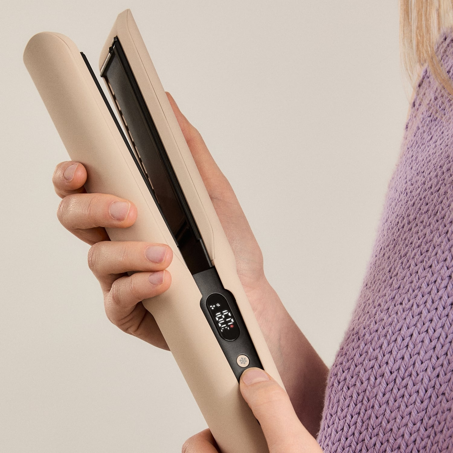 Una persona con un suéter morado sostiene una plancha de pelo beige con pantalla digital.