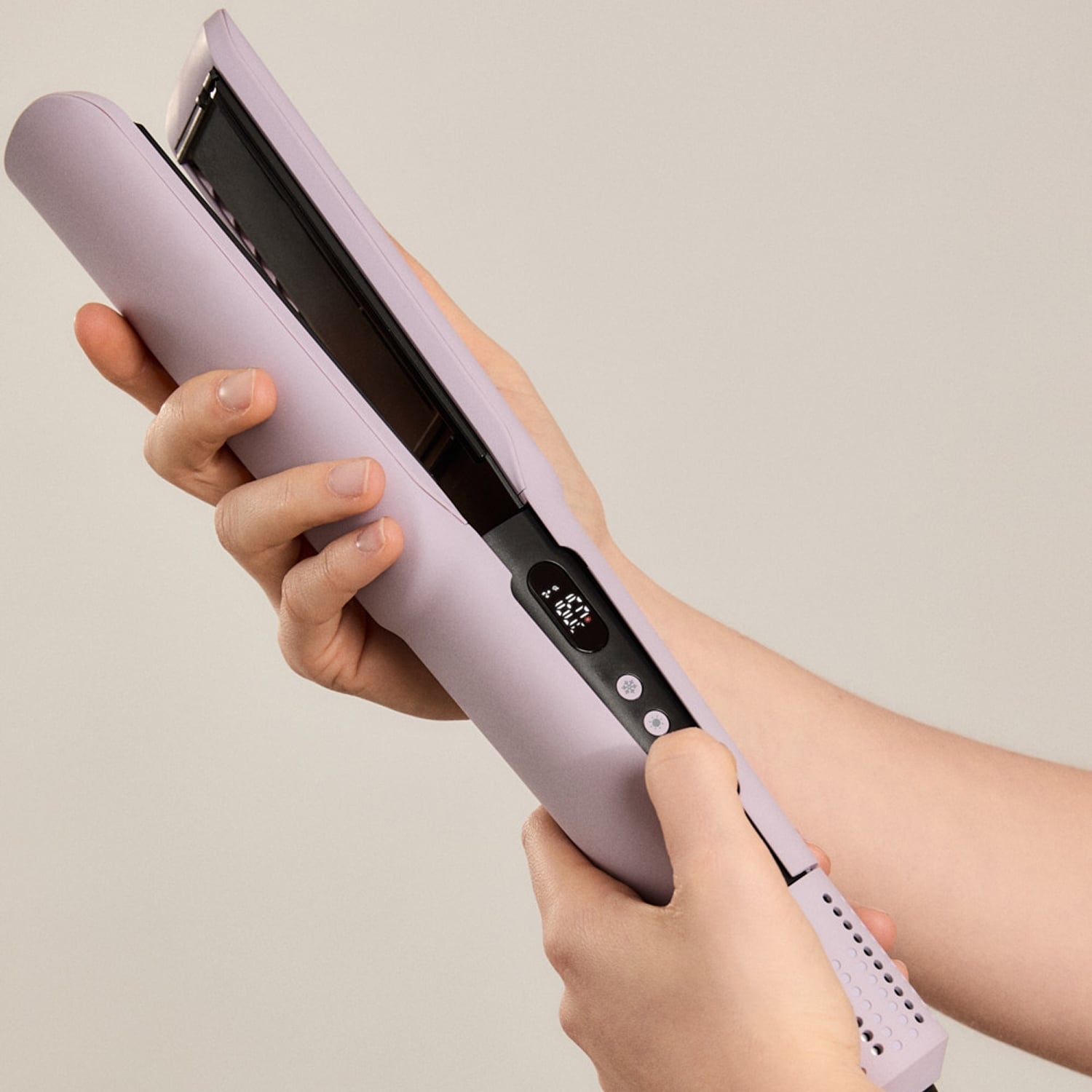 Una persona sostiene una plancha de pelo lavanda abierta con pantalla digital y botones.