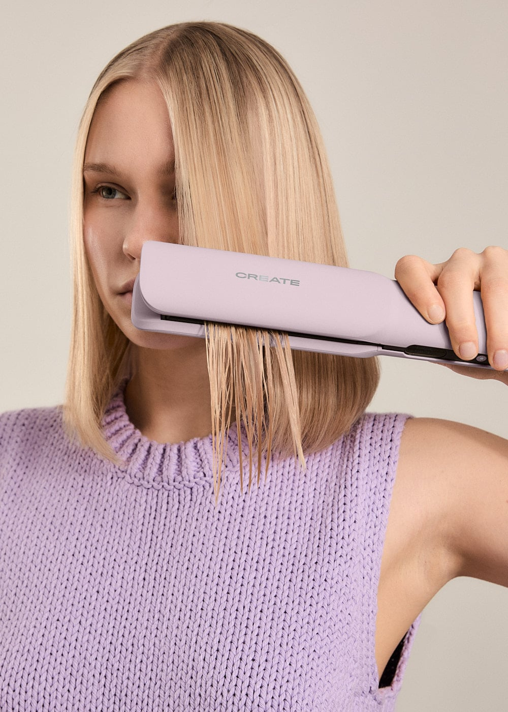 Una mujer rubia con top morado usa una plancha de pelo morada en cabello mojado.