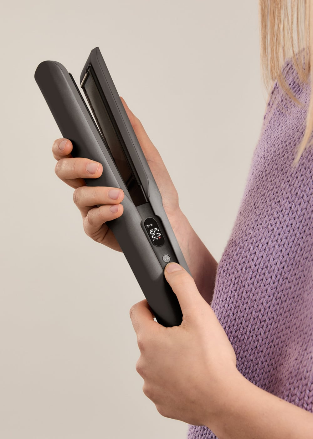 Una mujer con un suéter morado sostiene una plancha de pelo negra con pantalla digital.