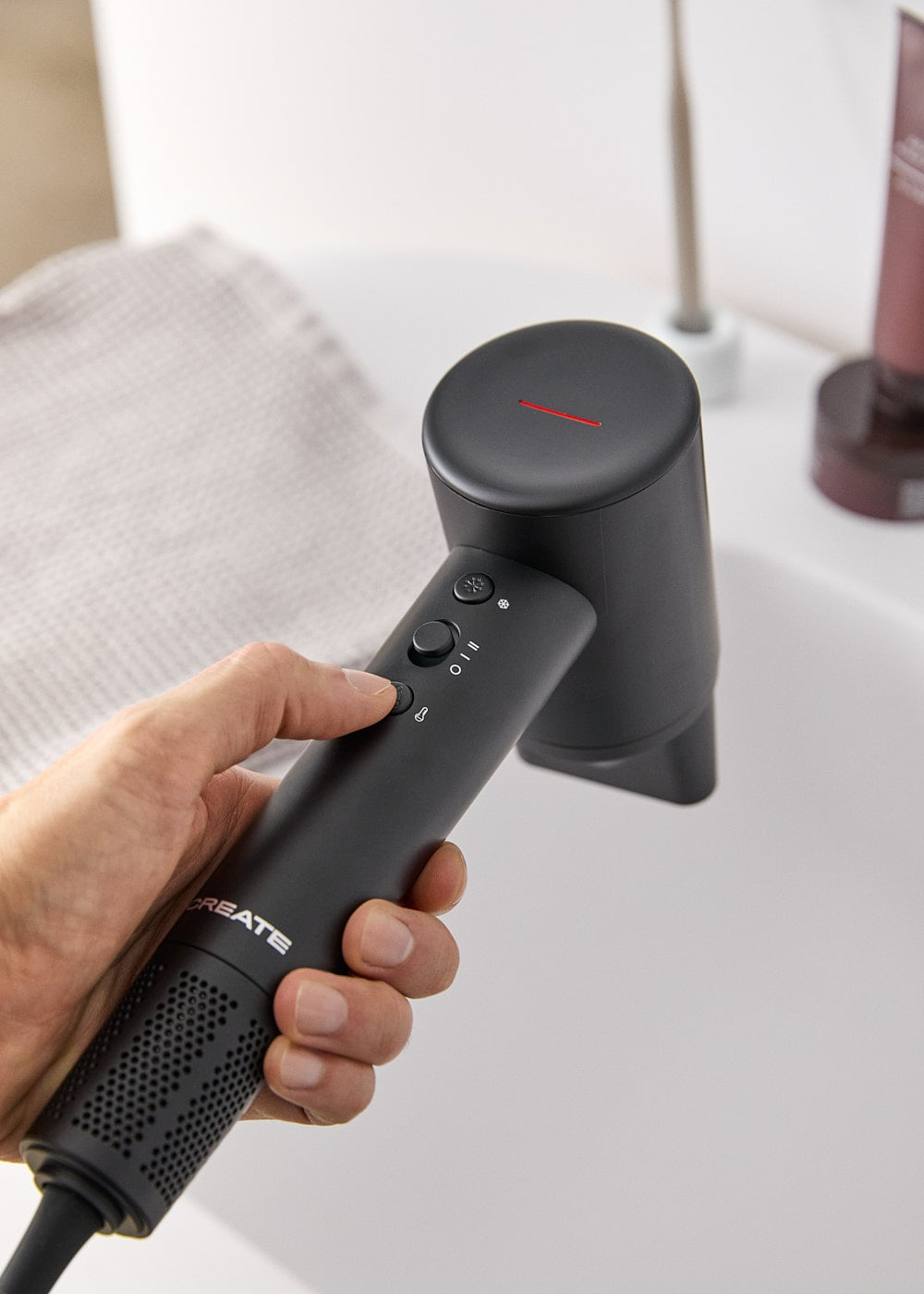 Una mano sostiene un secador de pelo negro moderno en un baño luminoso.