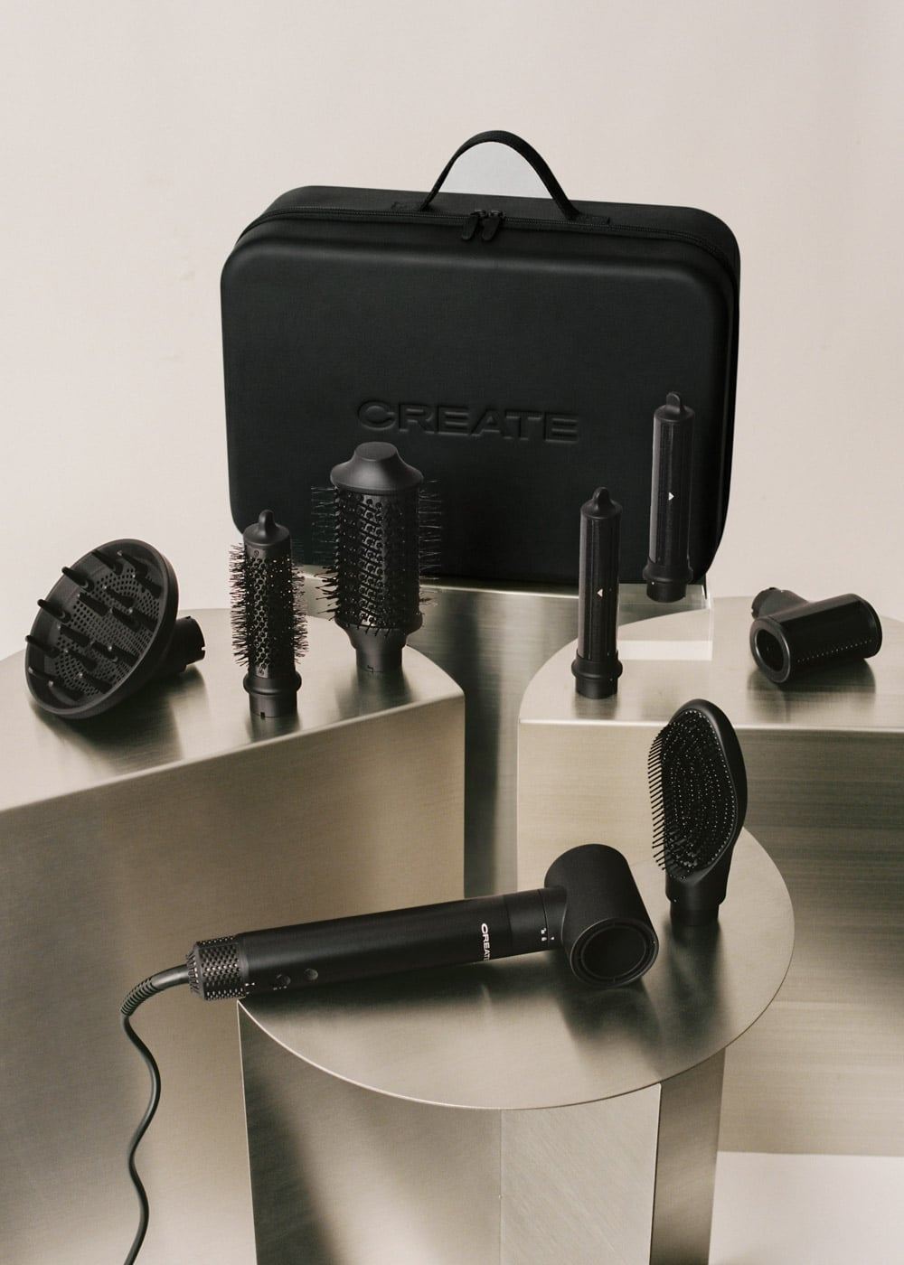 Set de secador de pelo negro con accesorios y estuche sobre pedestales metálicos con fondo claro.