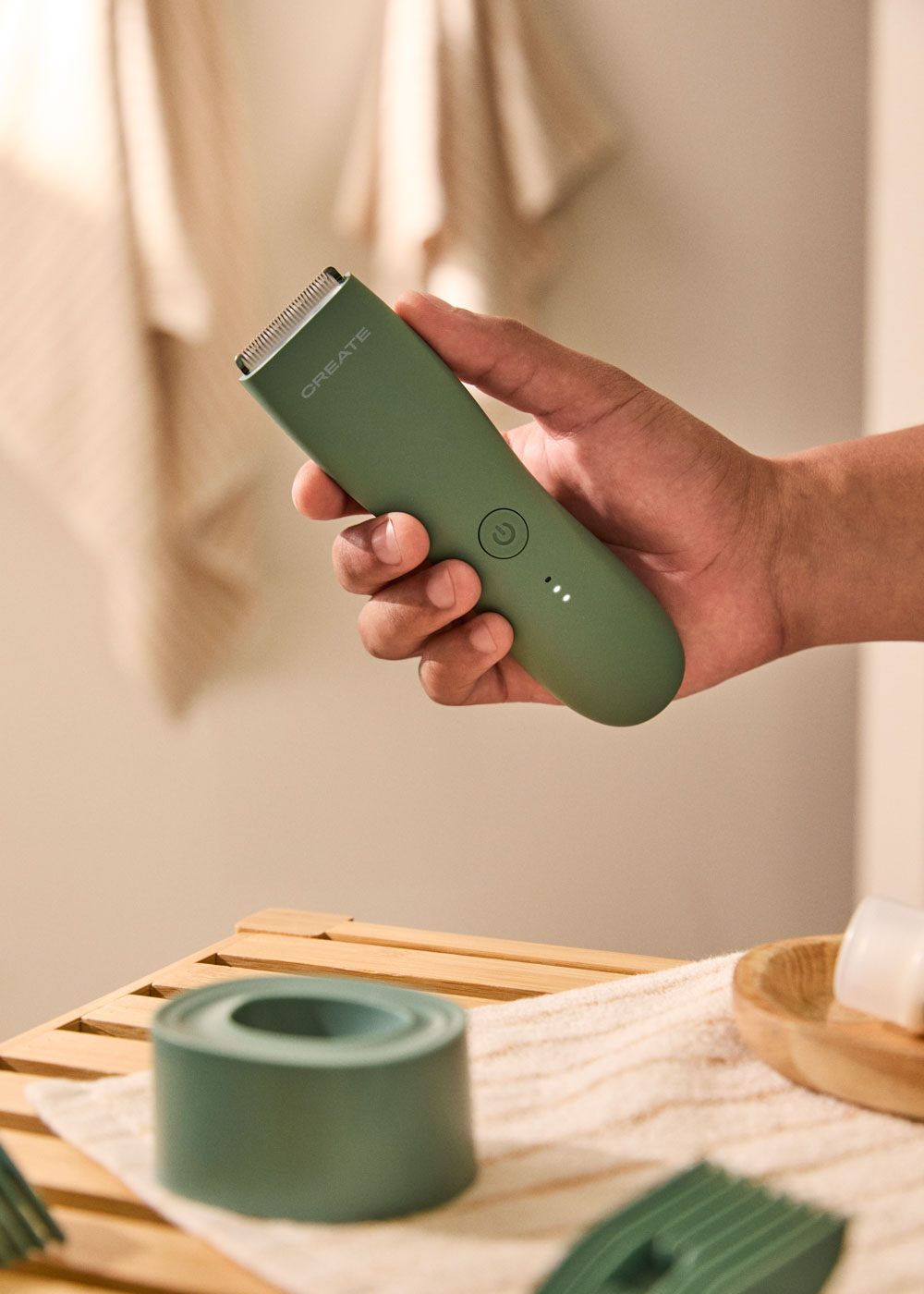 Una mano sostiene una cortapelos verde frente a un fondo de baño con accesorios.