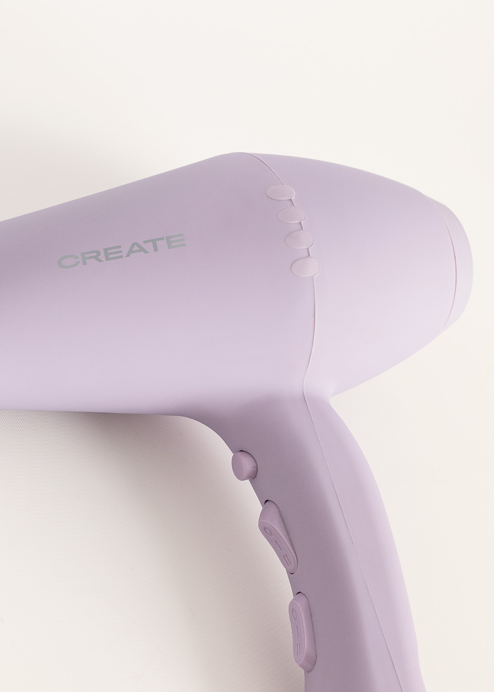 Un secador de pelo morado con la marca Create en gris en el lateral, sobre un fondo claro.