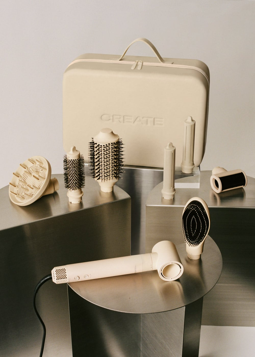 Un secador de pelo beige con varios accesorios y un estuche de viaje a juego sobre pedestales.