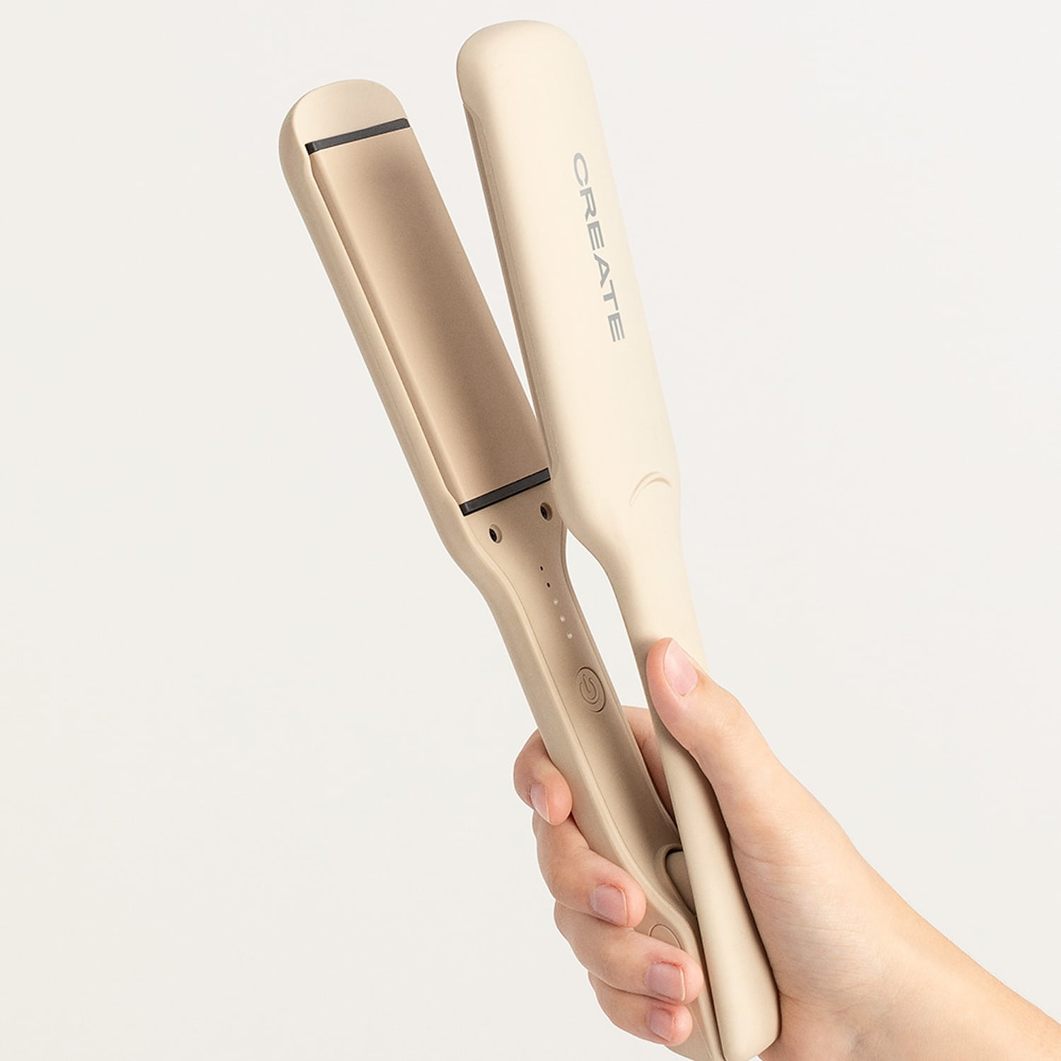 Una mano sostiene una plancha de pelo inalámbrica abierta y beige contra un fondo claro.