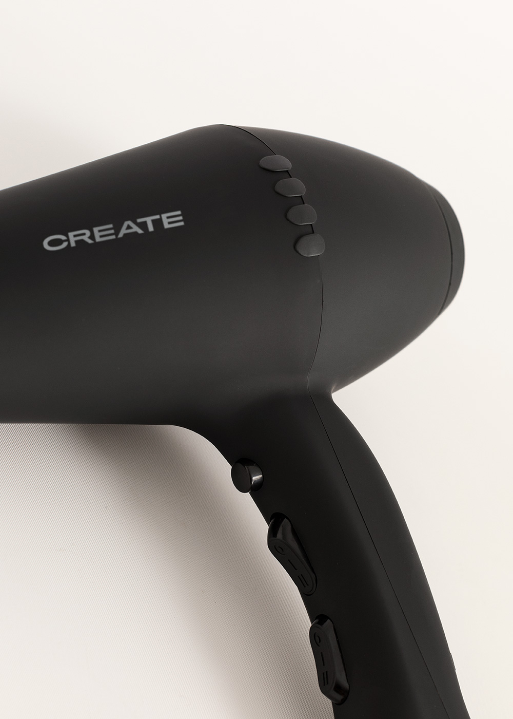 Un secador de pelo negro CREATE con botones superiores e interruptores en el mango sobre fondo blanco.