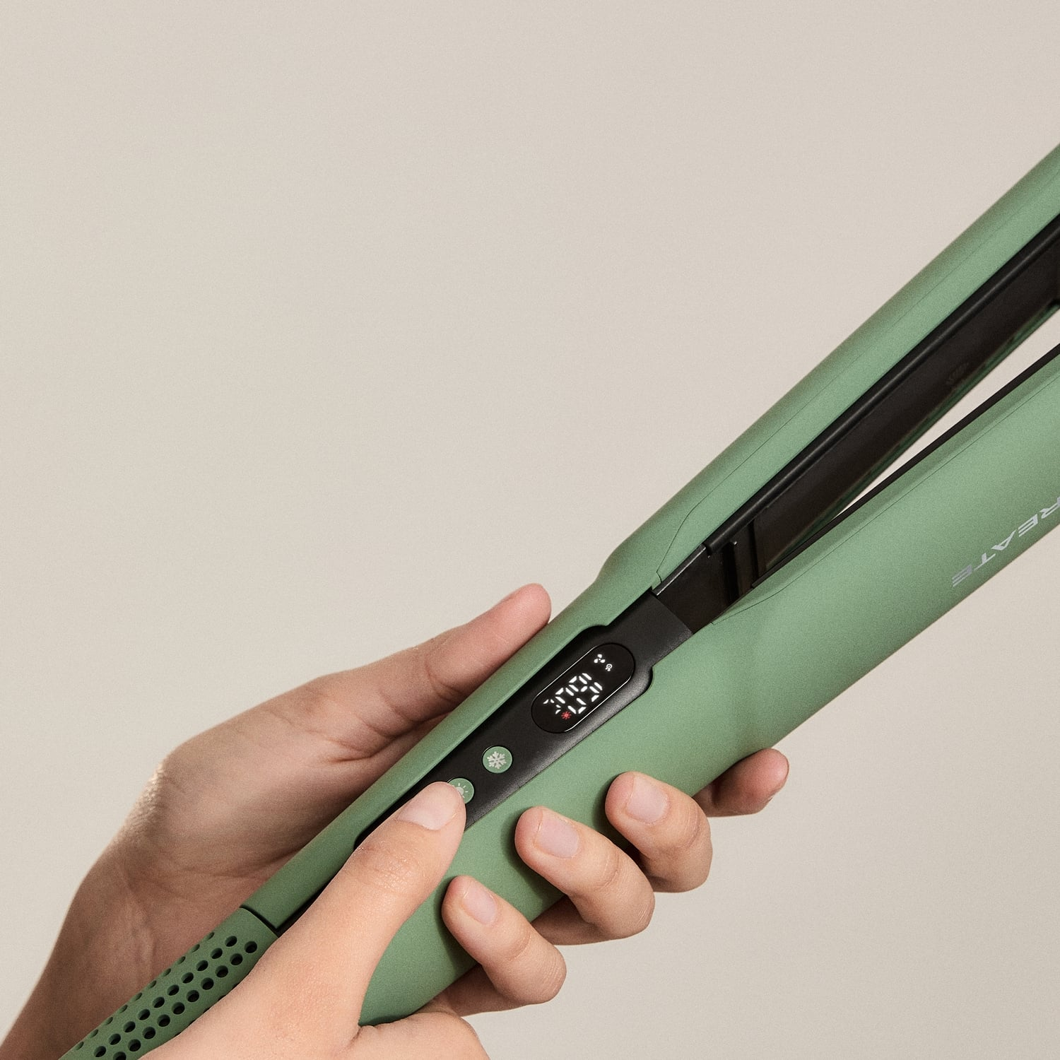 Manos sosteniendo una plancha de pelo verde salvia con pantalla digital y botones de control.