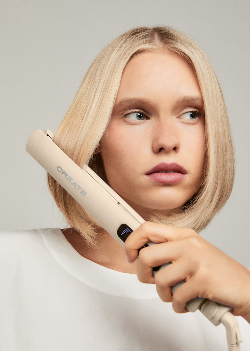 Una mujer rubia usa una plancha de pelo CREATE beige en su cabello lacio.