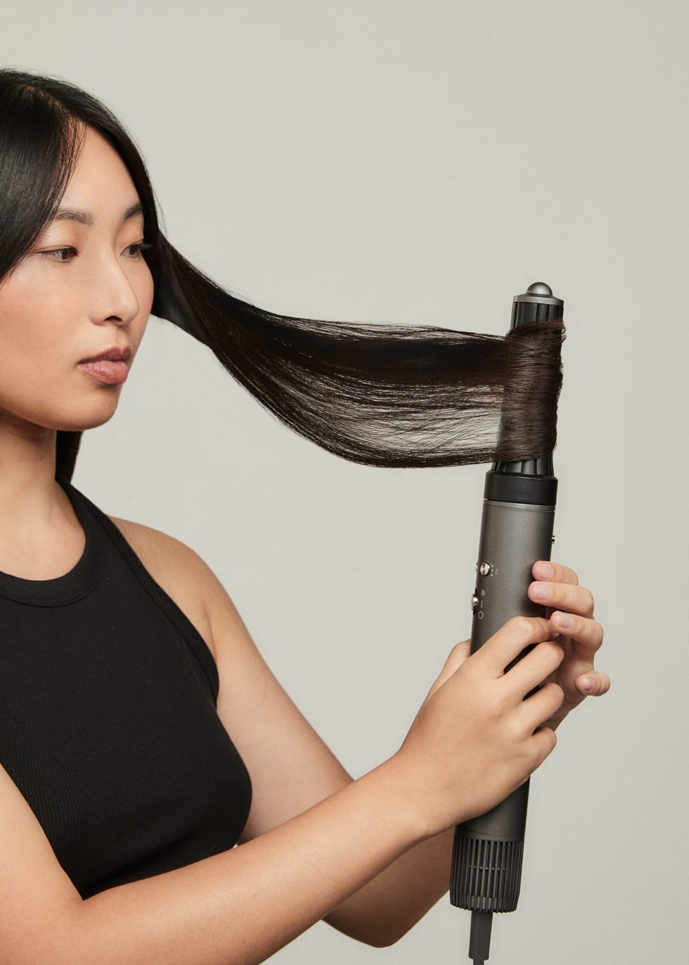 Una mujer con cabello negro y largo envuelve un mechón alrededor de un rizador gris.