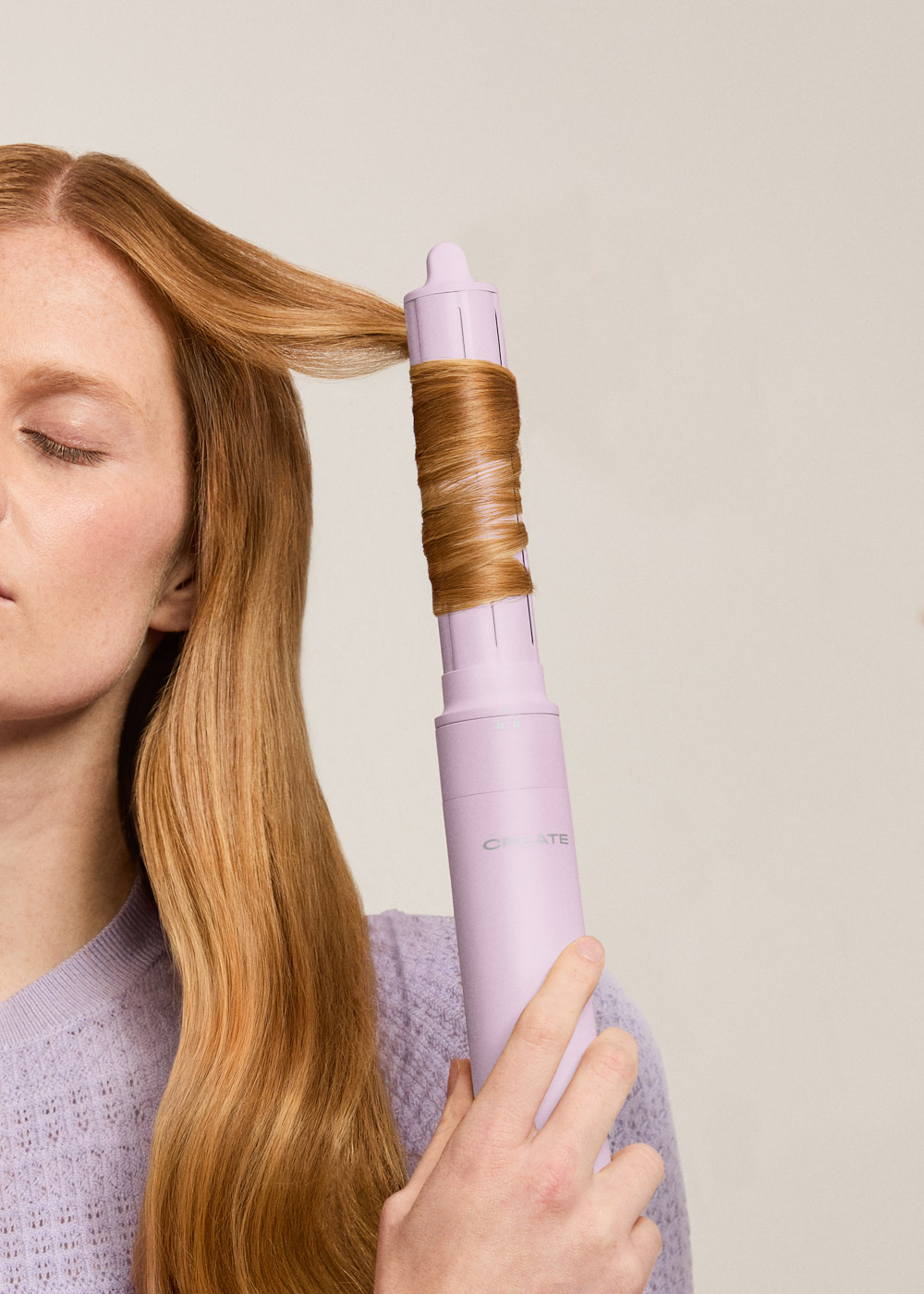 Una mujer sostiene una rizadora lila clara con un mechón de cabello rubio enrollado.