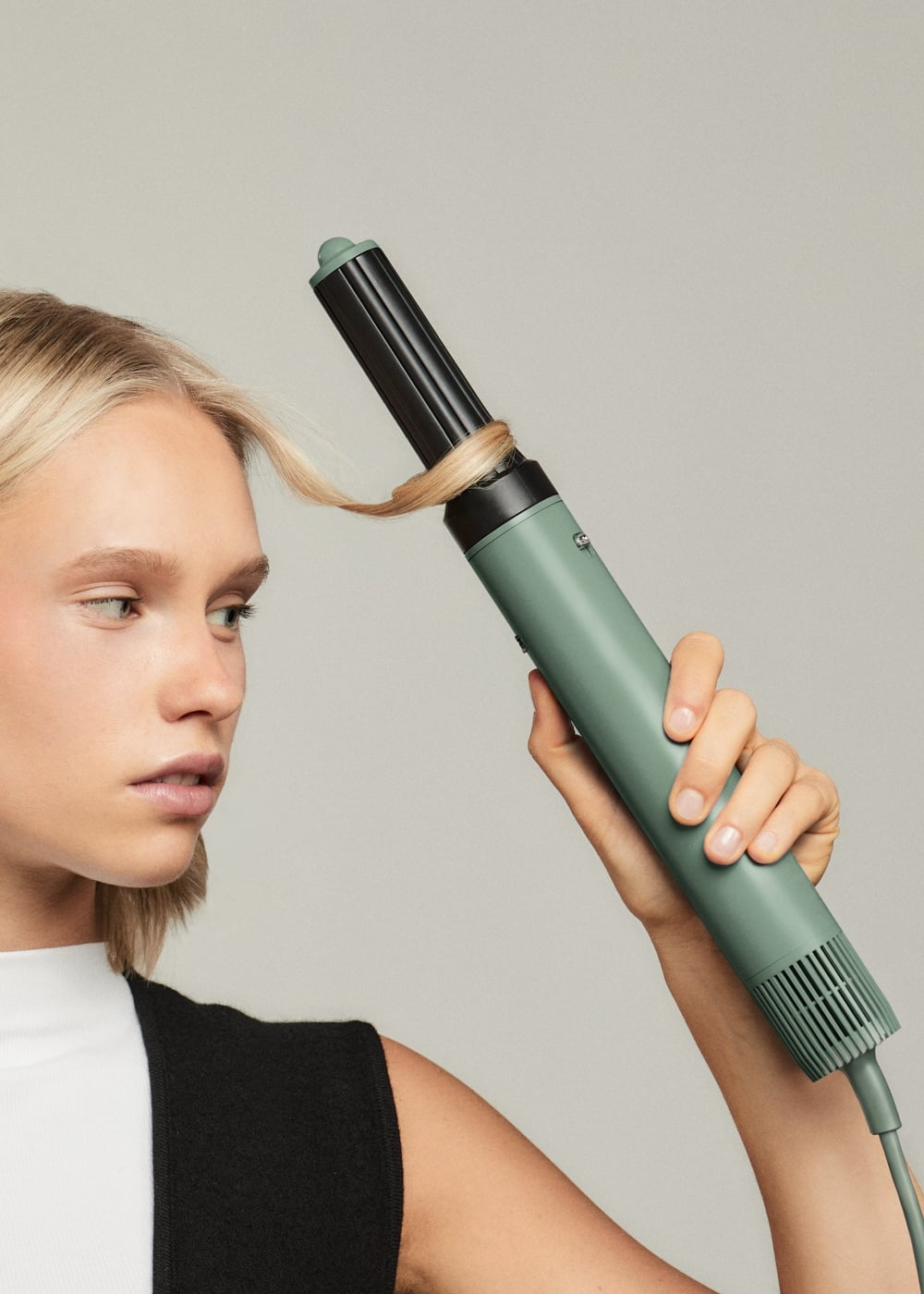 Una mujer rubia se peina el cabello con un rizador verde menta.