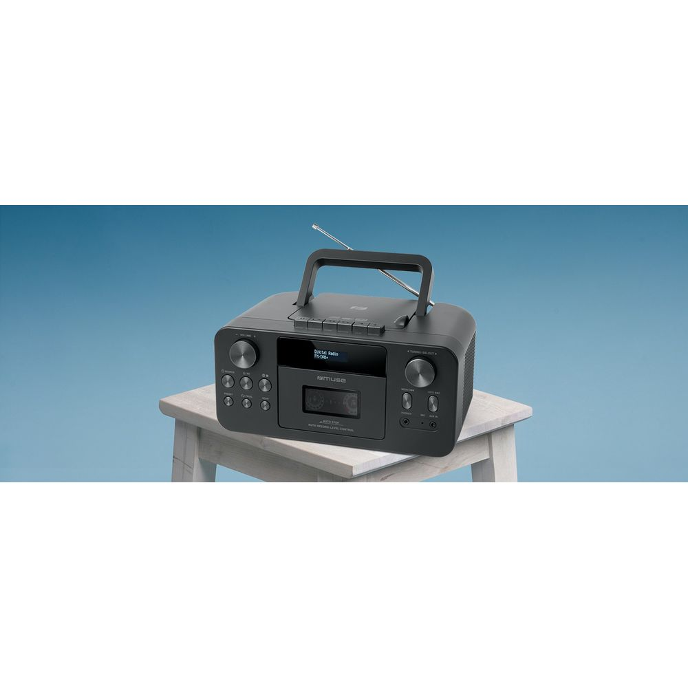 Ein schwarzer Ghettoblaster mit Kassetten- und Radioteil steht auf einem hellen Holzhocker vor hellblauem Hintergrund.
