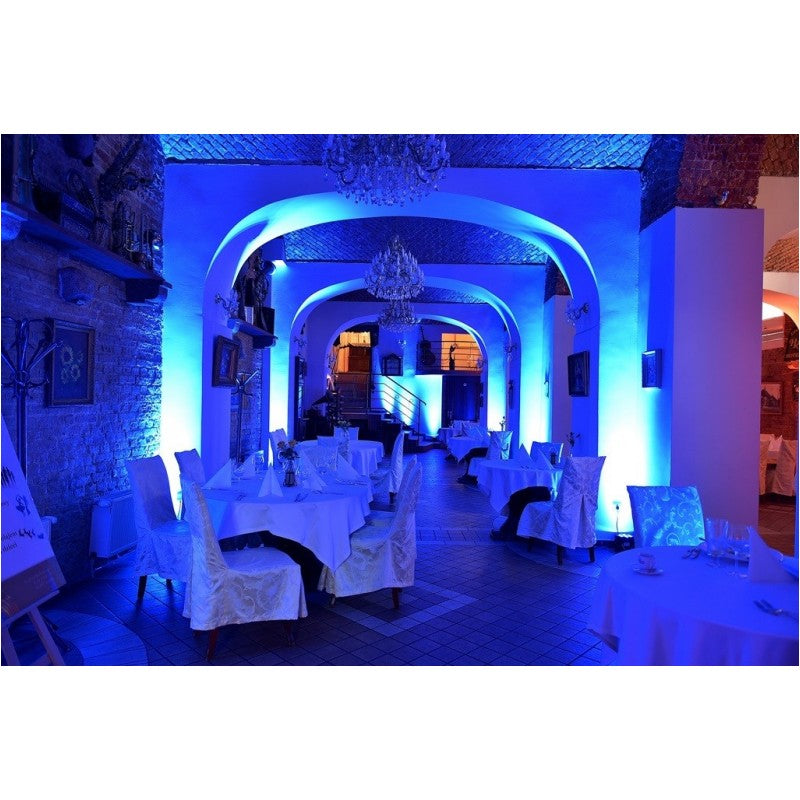 Ein Restaurant interior beleuchtet mit blauem Licht, weißen Tischdecken und Kronleuchtern an der Decke.