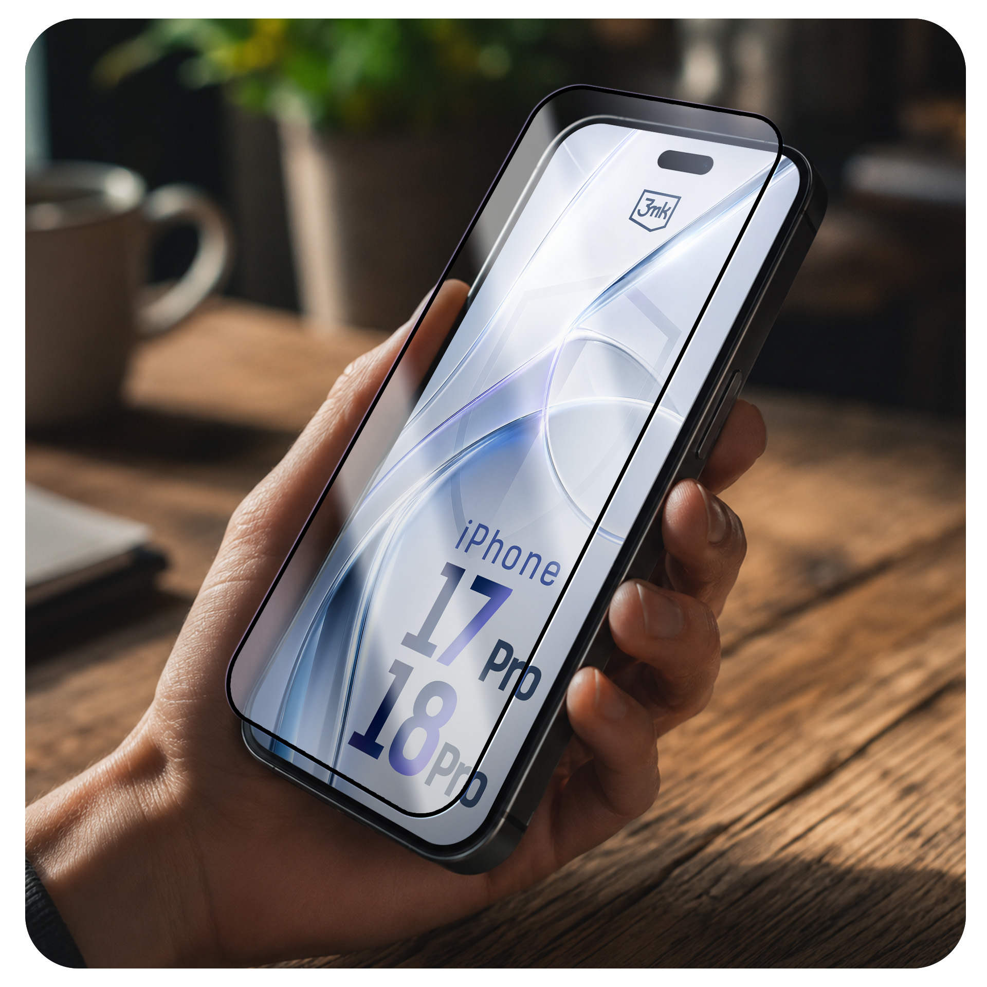 Ręka trzymająca smartfon z folią ochronną na drewnianym stole.