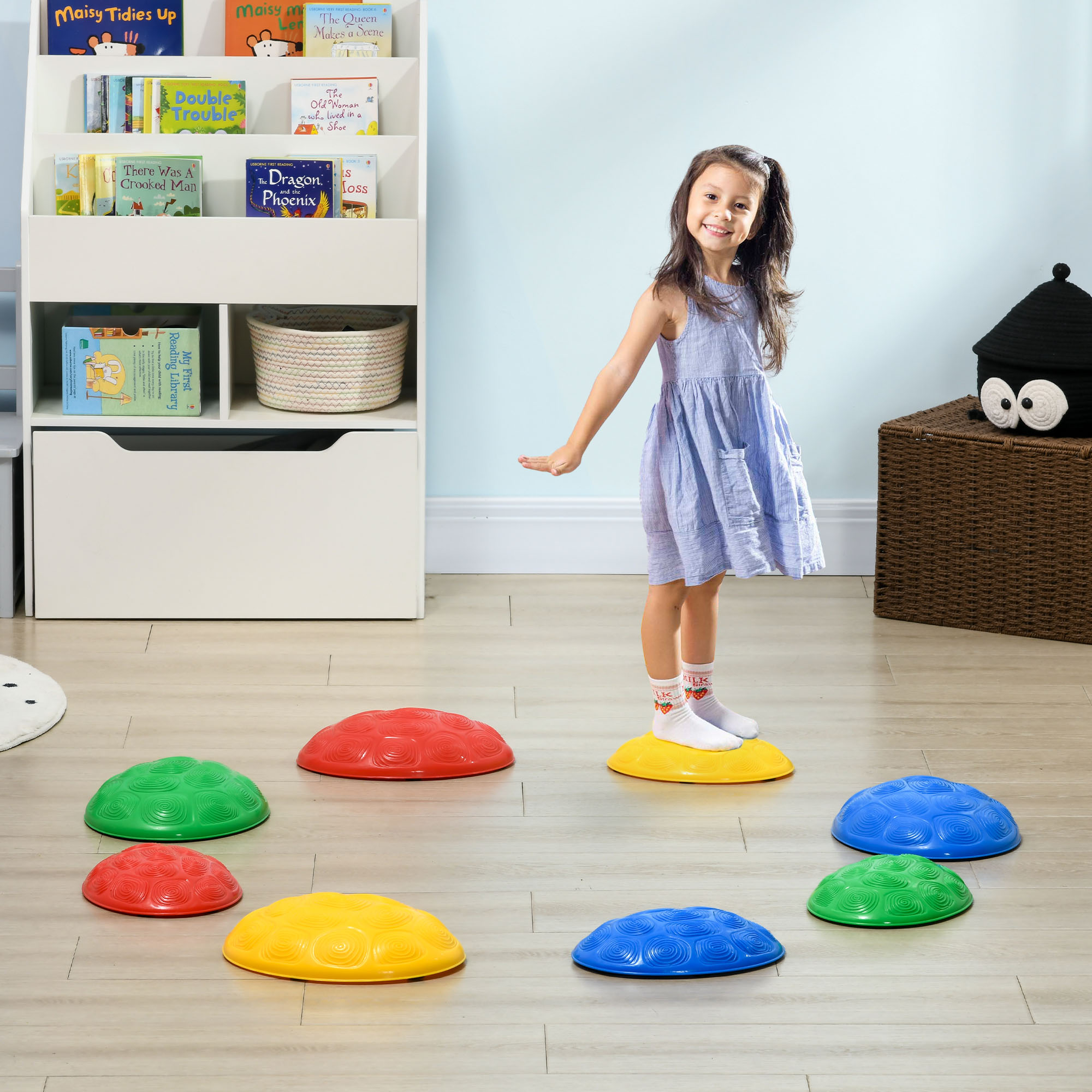 Una niña con un vestido azul hace equilibrio sobre juguetes de cúpula de colores.