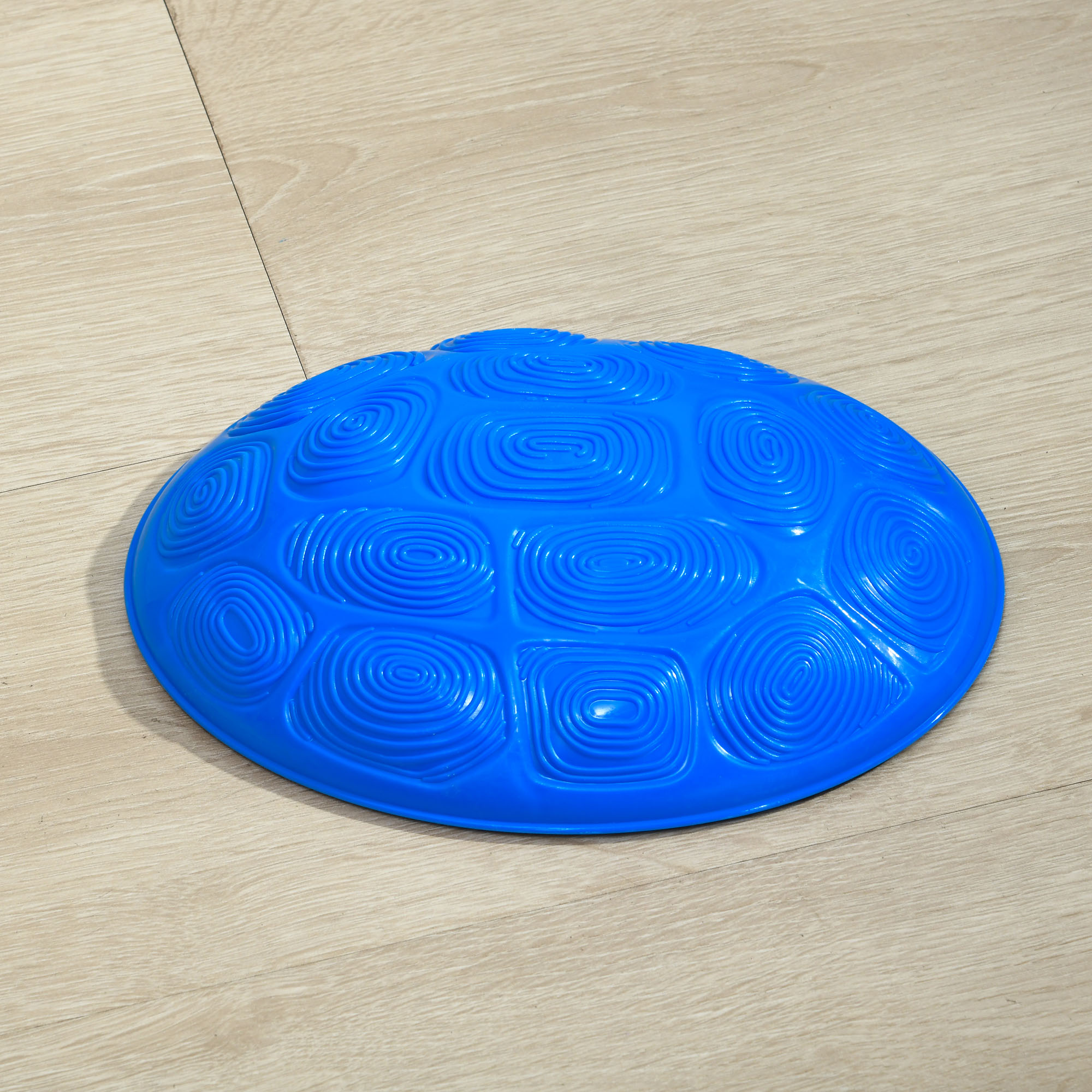 Una piedra de equilibrio sensorial azul en forma de cúpula con patrones en espiral descansa sobre un suelo de madera clara.