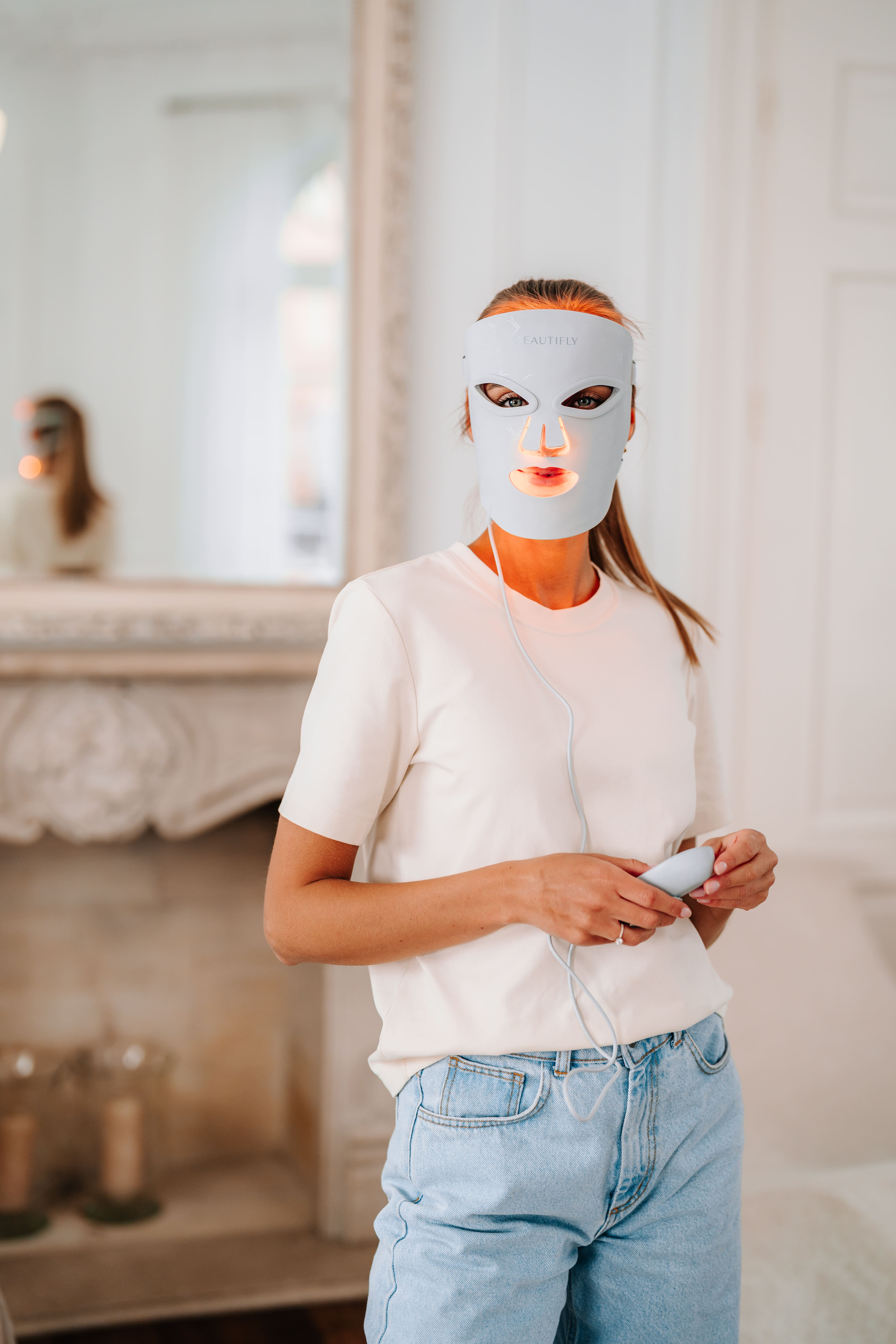 Kobieta w białym t-shircie nosi białą maskę LED na twarz z pomarańczowym światłem.