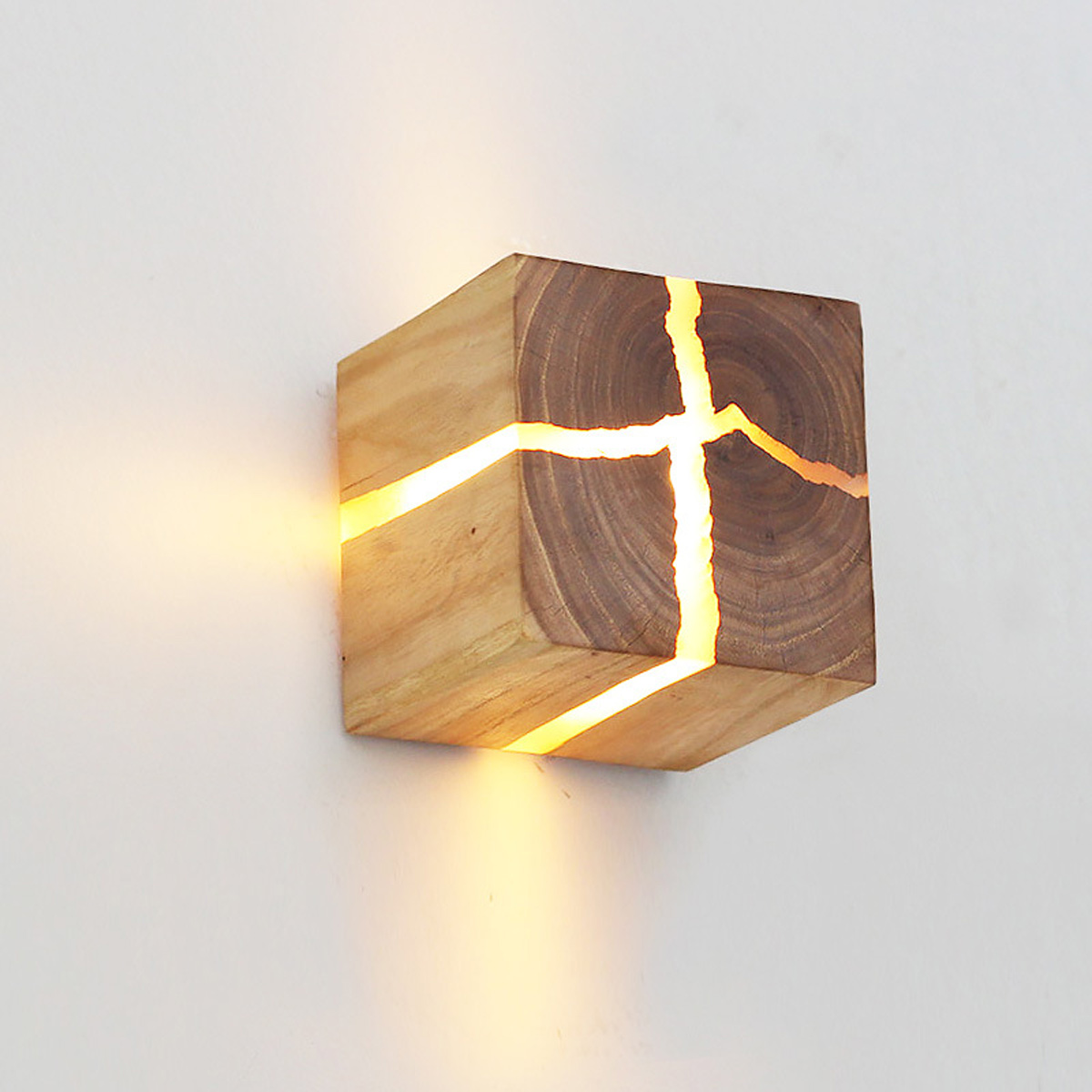 Eine quadratische Holzwandleuchte mit leuchtenden Rissen an einer weißen Wand.