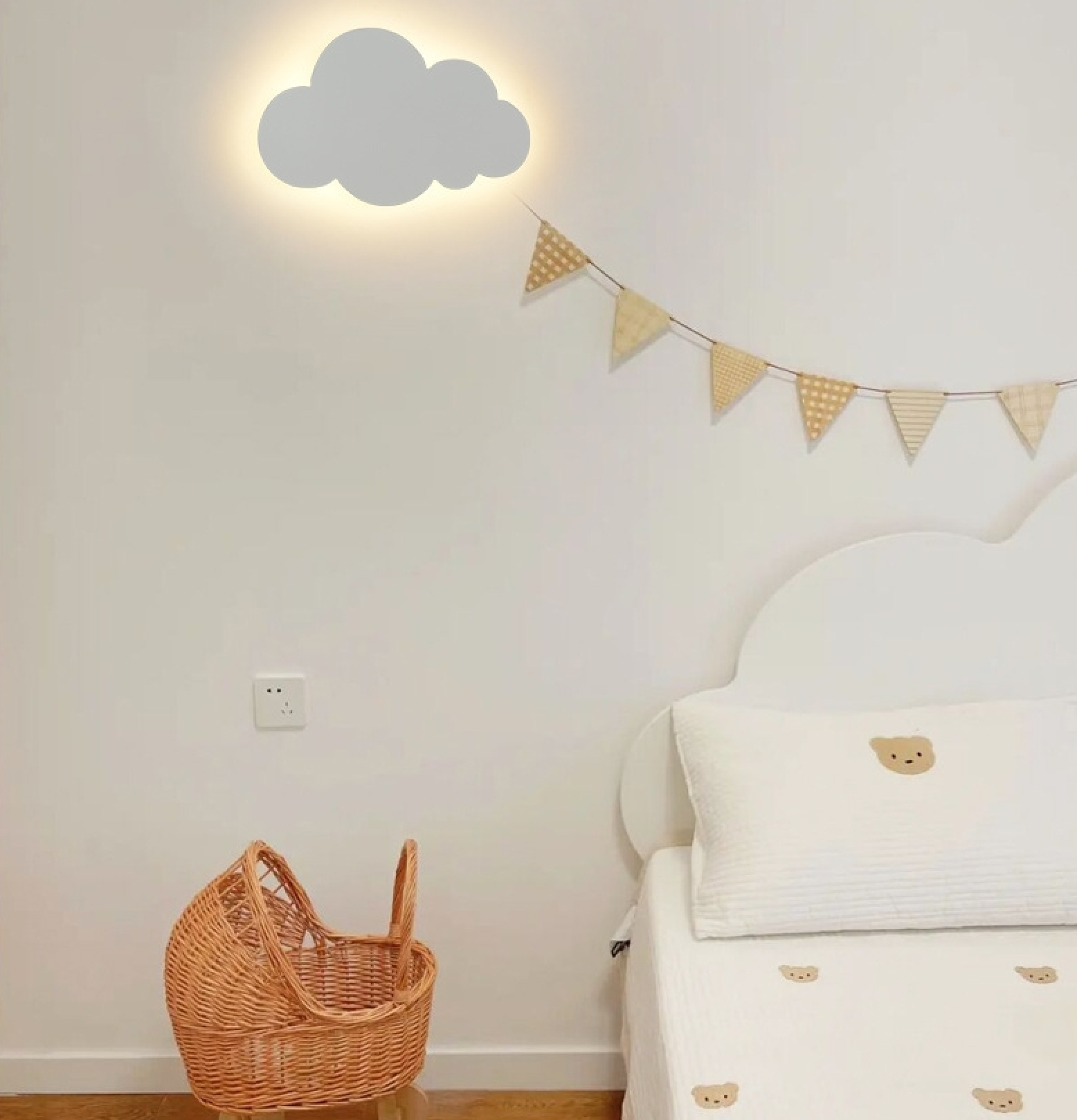 Ein Kinderzimmer mit grauer Wolkenlampe, Wimpelkette, weißem Bett mit Bärenmotiven und einem Rattankorb auf dem Boden.