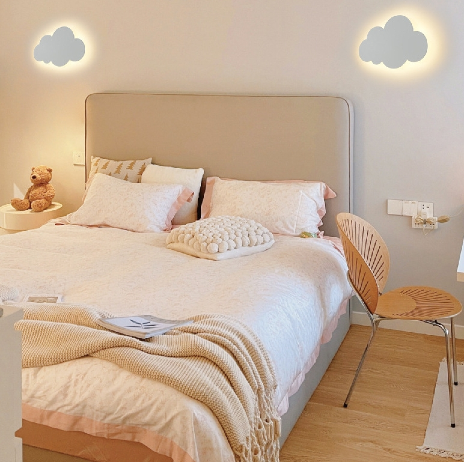 Gemütliches Schlafzimmer mit großem Bett, Plüschtier, Holzsessel und zwei leuchtenden Wolkenlampen an der Wand.