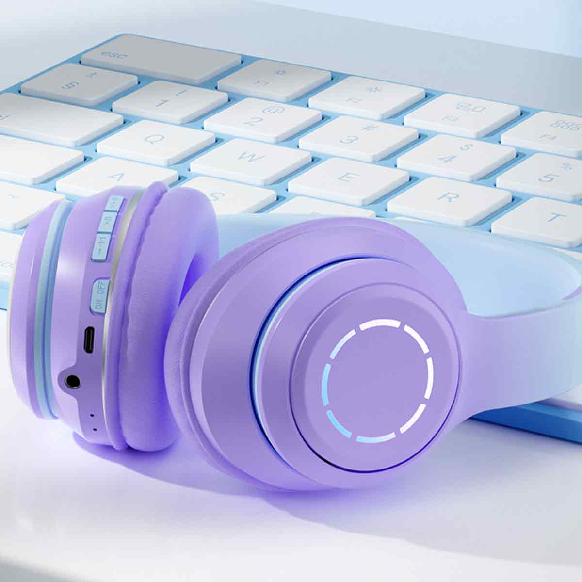 Lila kabellose Kopfhörer liegen vor einer hellblauen Tastatur auf einer weißen Oberfläche.