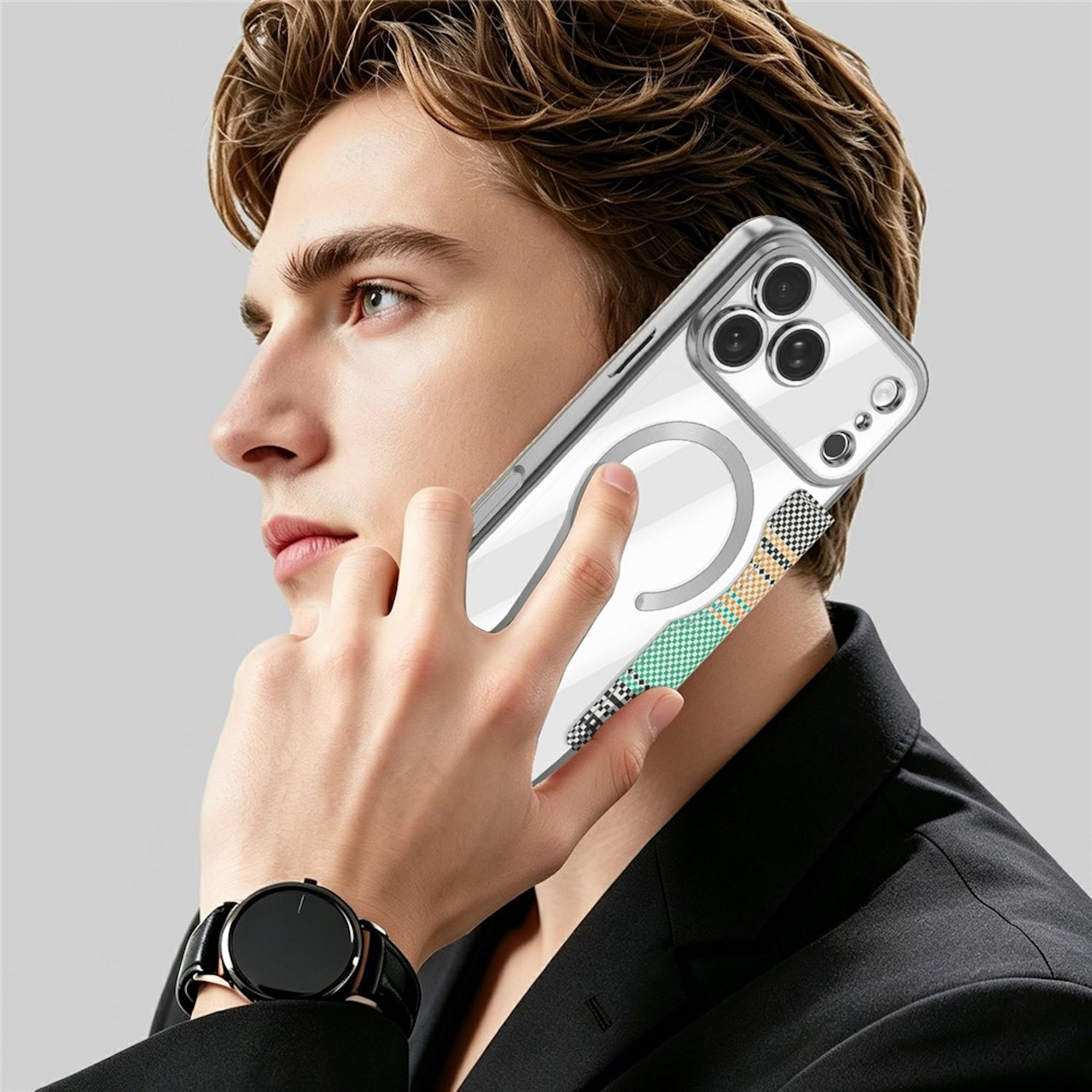 Ein junger Mann im schwarzen Blazer telefoniert mit einem klaren iPhone mit gemustertem Band und schwarzer Armbanduhr.