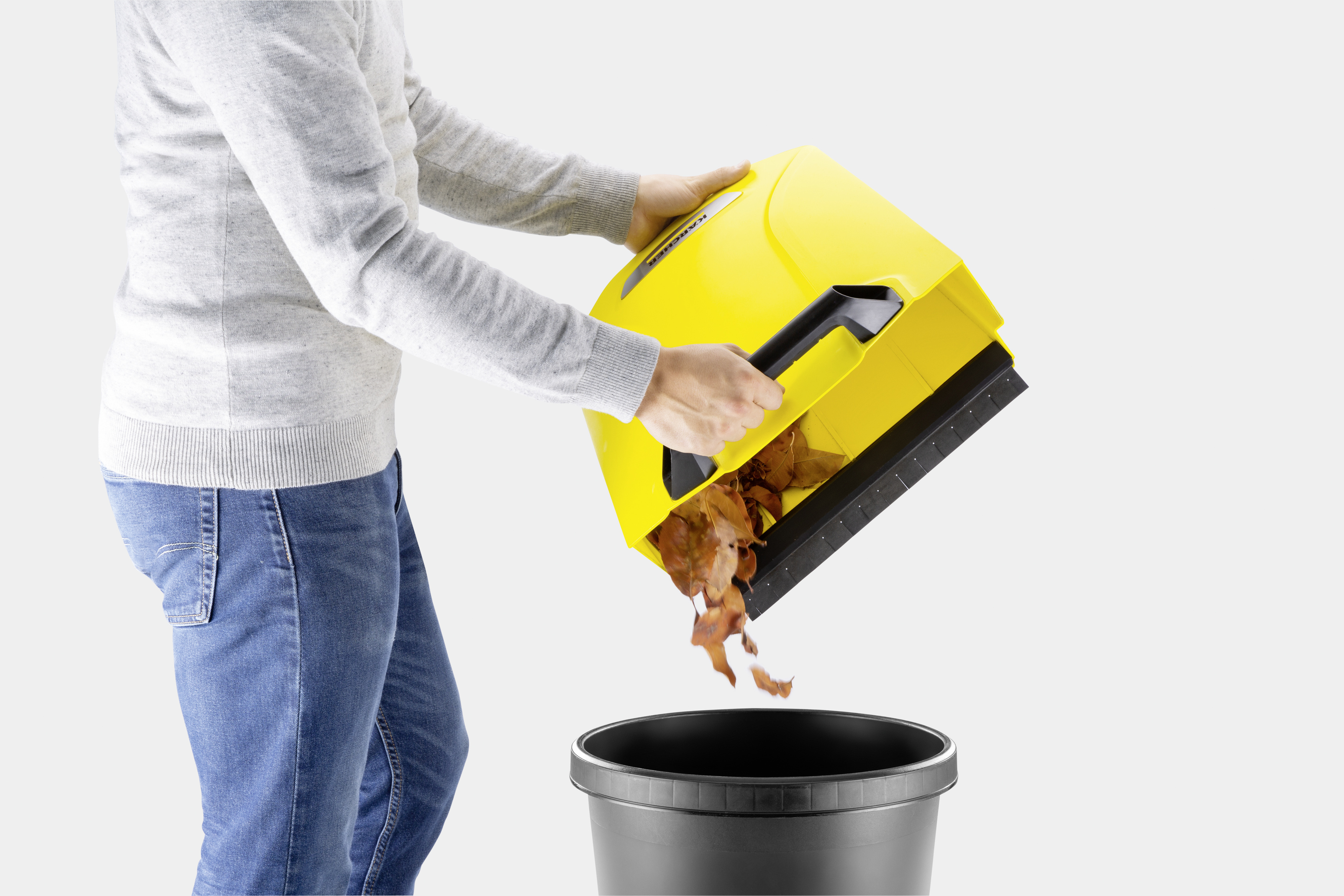 Una persona vacía hojas secas de un dispositivo de barrido amarillo en un cubo negro.
